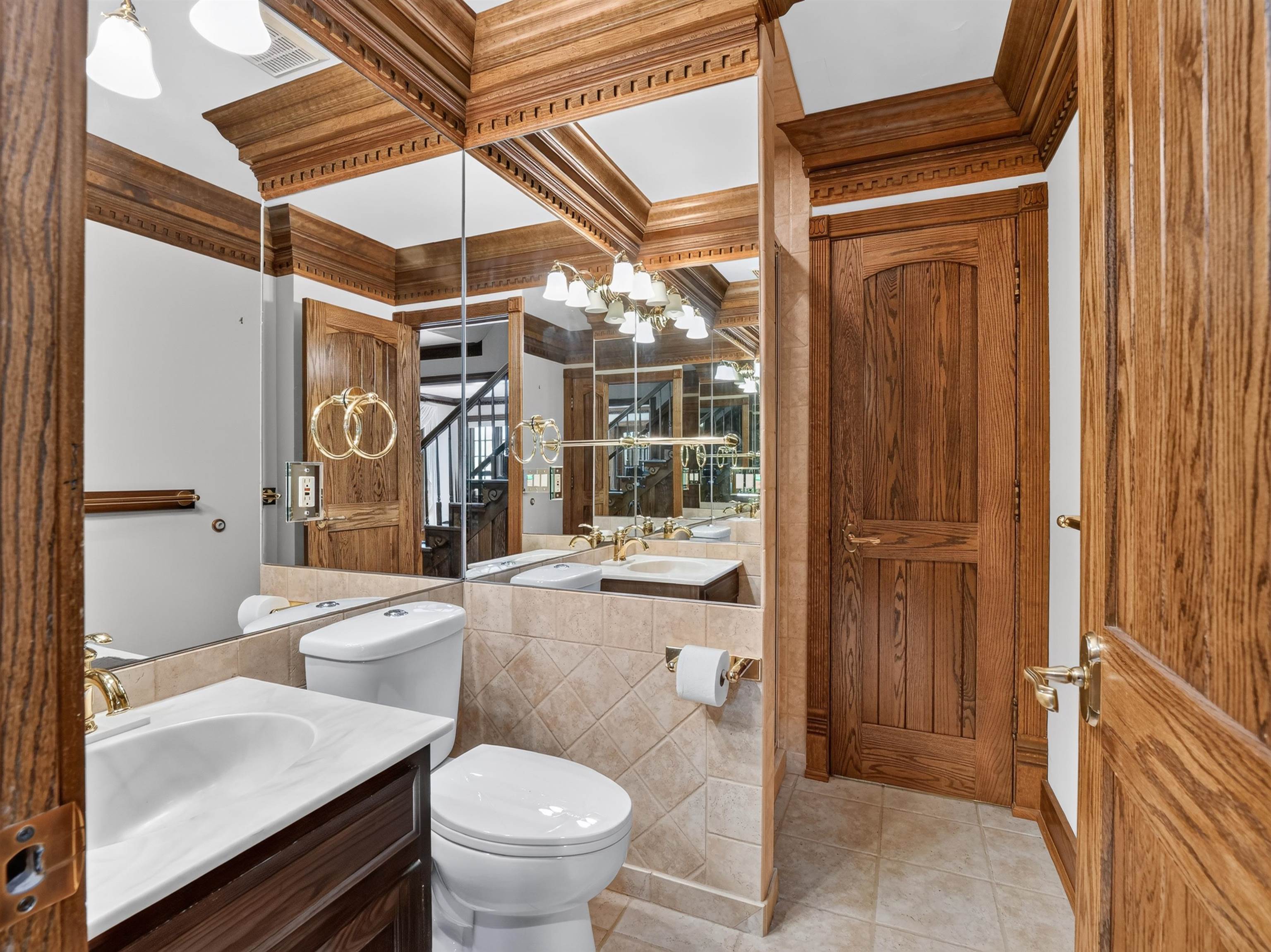 Powder room featuring extensive wood trim, full-height wall mirrors, a toilet, a vanity with a white countertop and integrated sink, and tile flooring