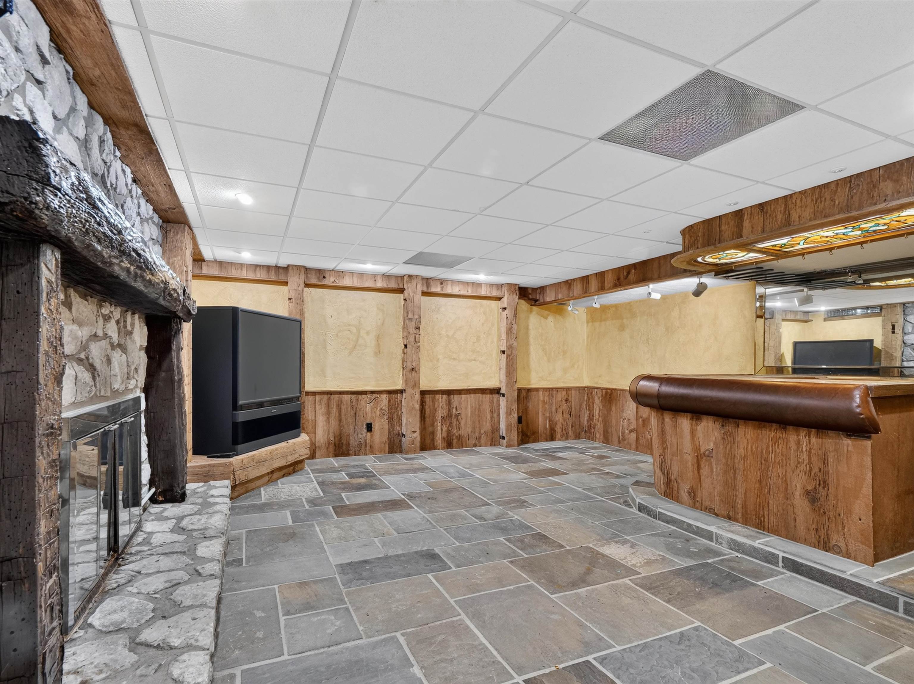 Spacious room featuring stone-finish flooring, a built-in wet bar, and a stone fireplace with a raised hearth