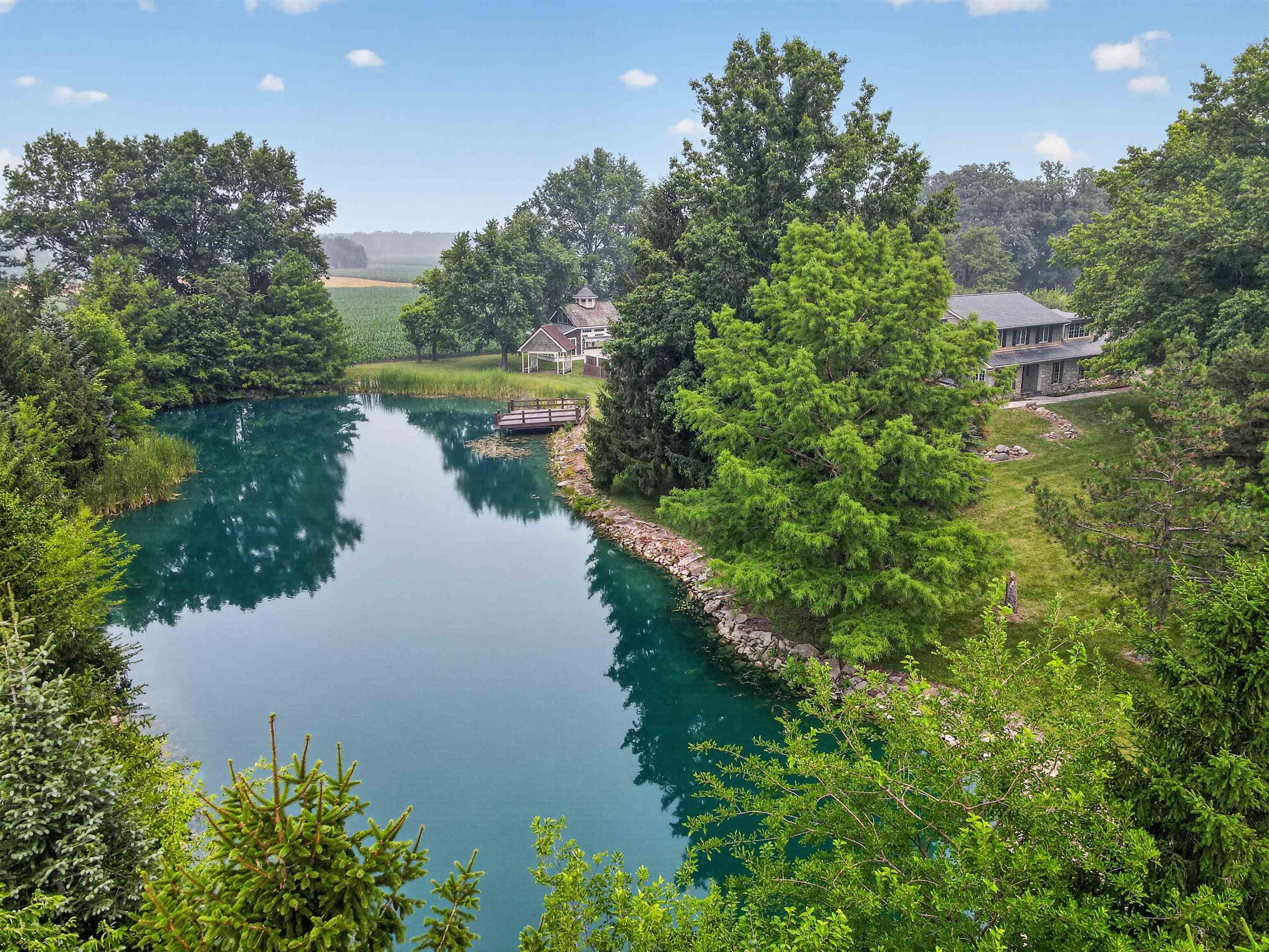 Expansive private pond with a wooden dock and natural rock-lined banks, surrounded by mature trees and lush greenery