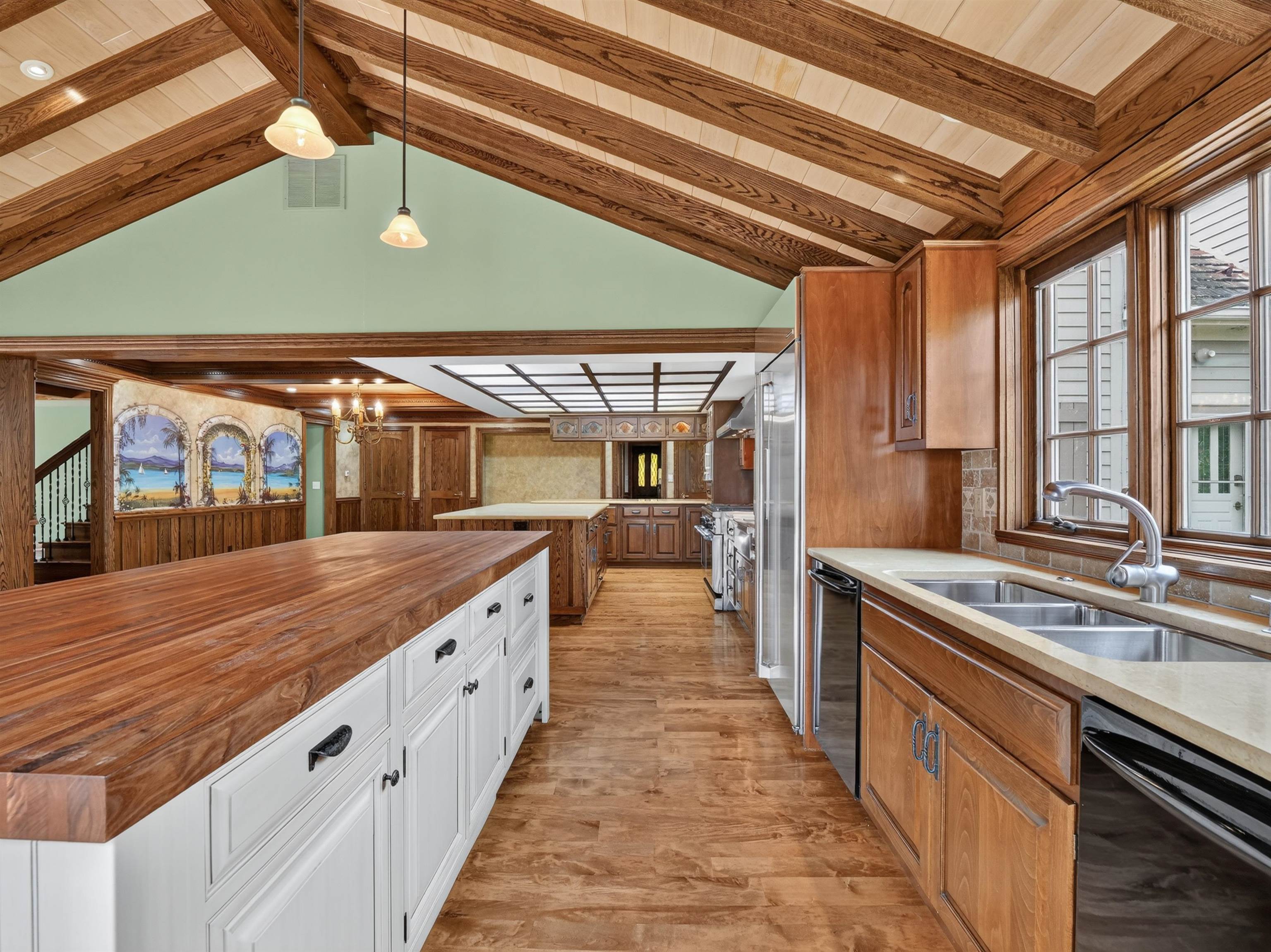 Kitchen featuring a vaulted wood-beam ceiling, wood-finish flooring, a double basin stainless steel sink, and light-toned countertops