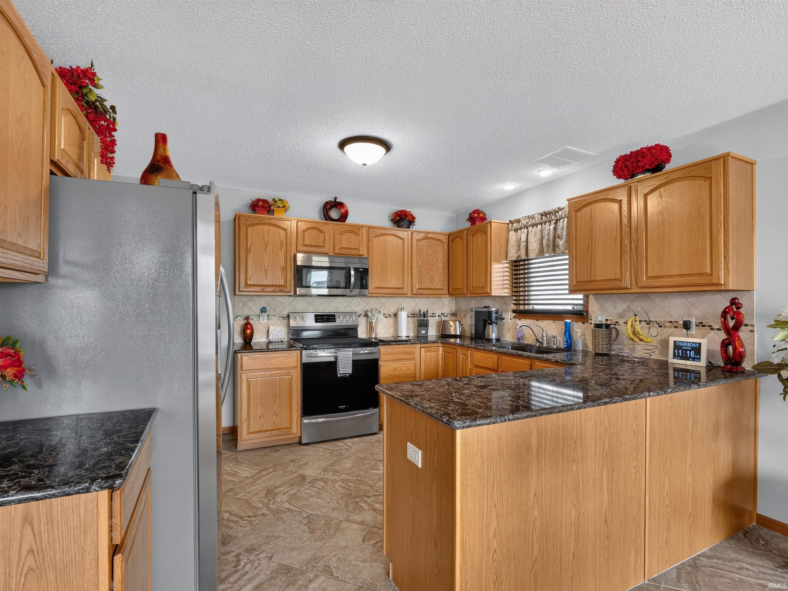 Kitchen featuring light wood cabinetry, dark granite-finish countertops, stainless steel appliances, and patterned tile flooring