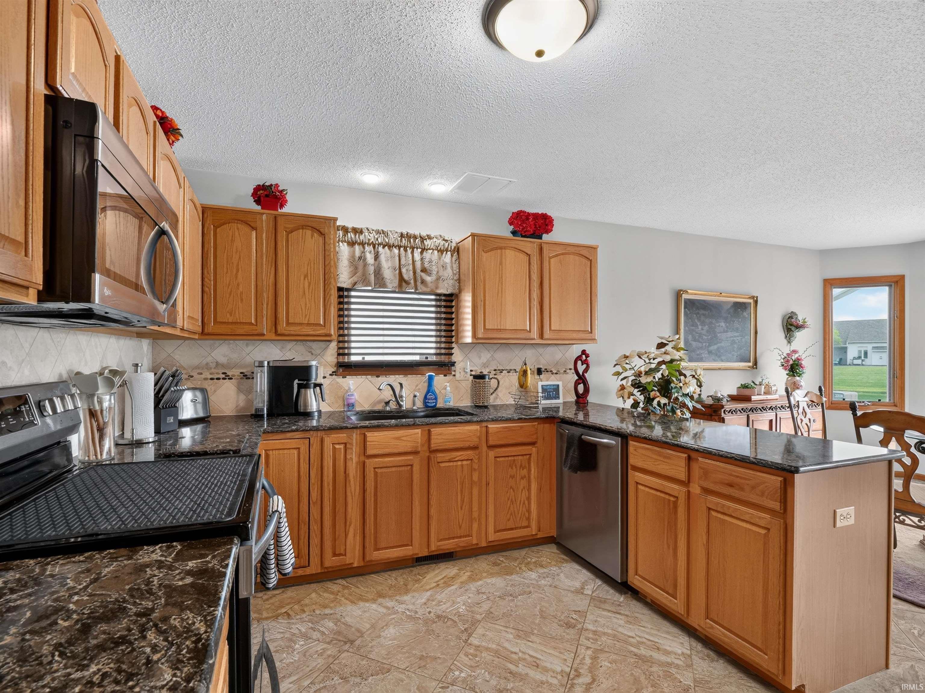 Kitchen featuring light wood cabinetry, dark patterned countertops, stainless steel appliances, and a tiled backsplash
