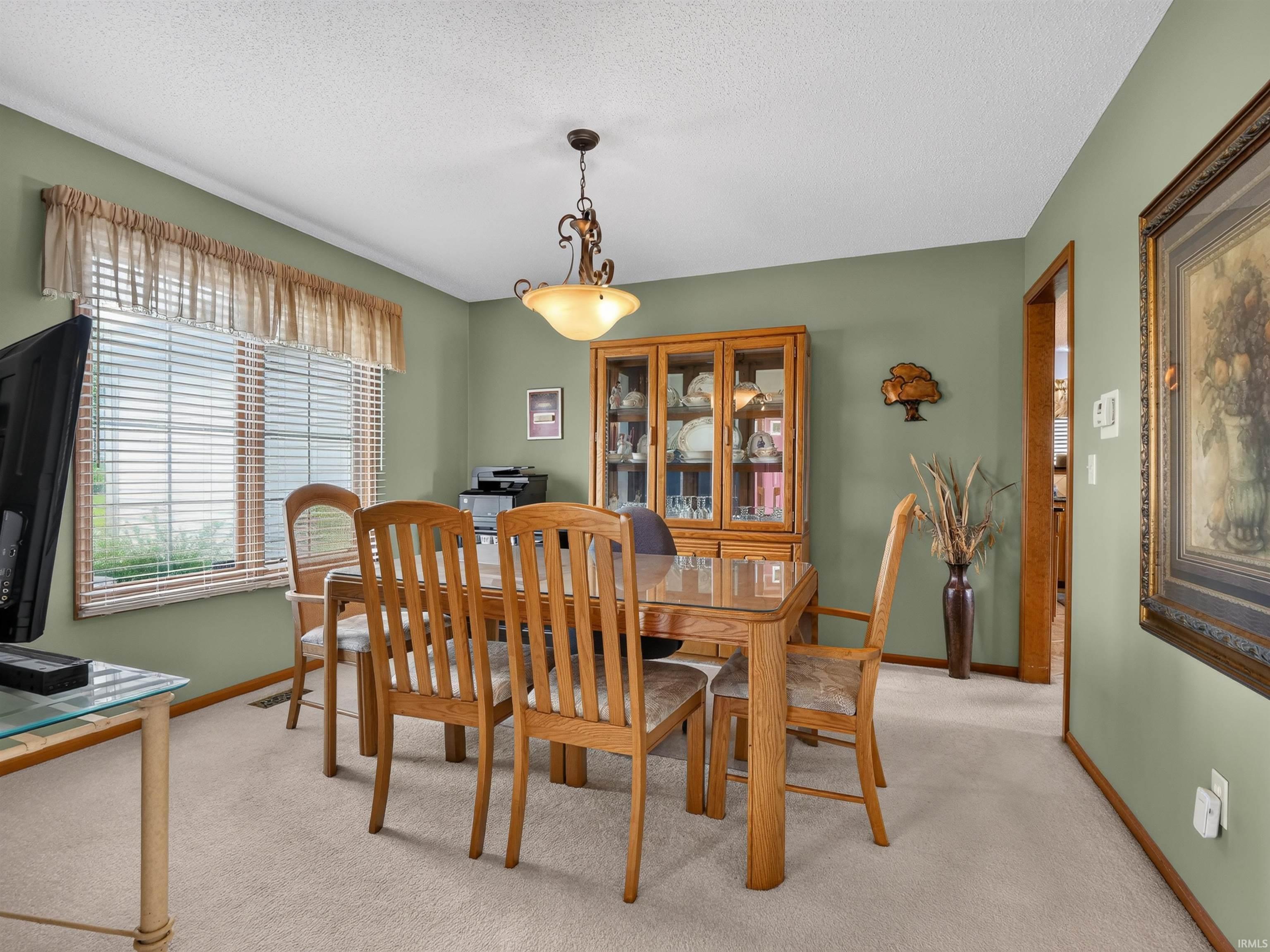 Dining area featuring light green walls, a window with blinds and valance, carpeted flooring, and a decorative ceiling fixture
