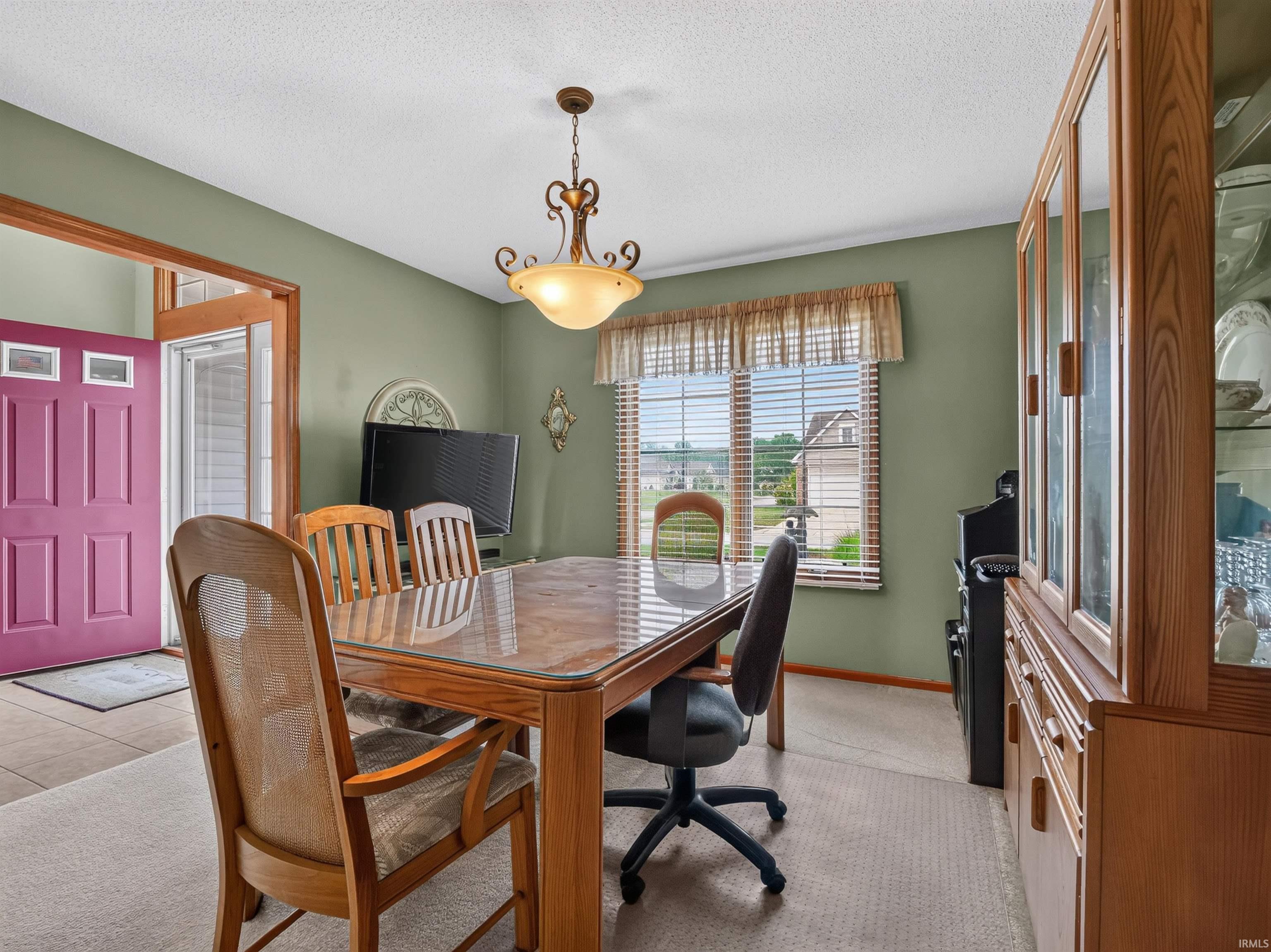 Dining area featuring a prominent window with horizontal blinds, neutral carpet flooring, and a decorative ceiling light fixture