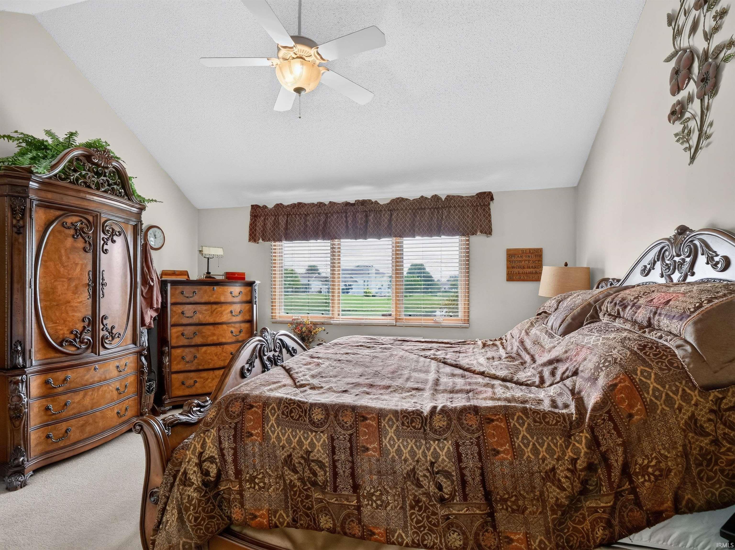 Vaulted ceiling bedroom featuring a ceiling fan with integrated lighting, twin windows with blinds, light-toned wall paint, and neutral carpeting