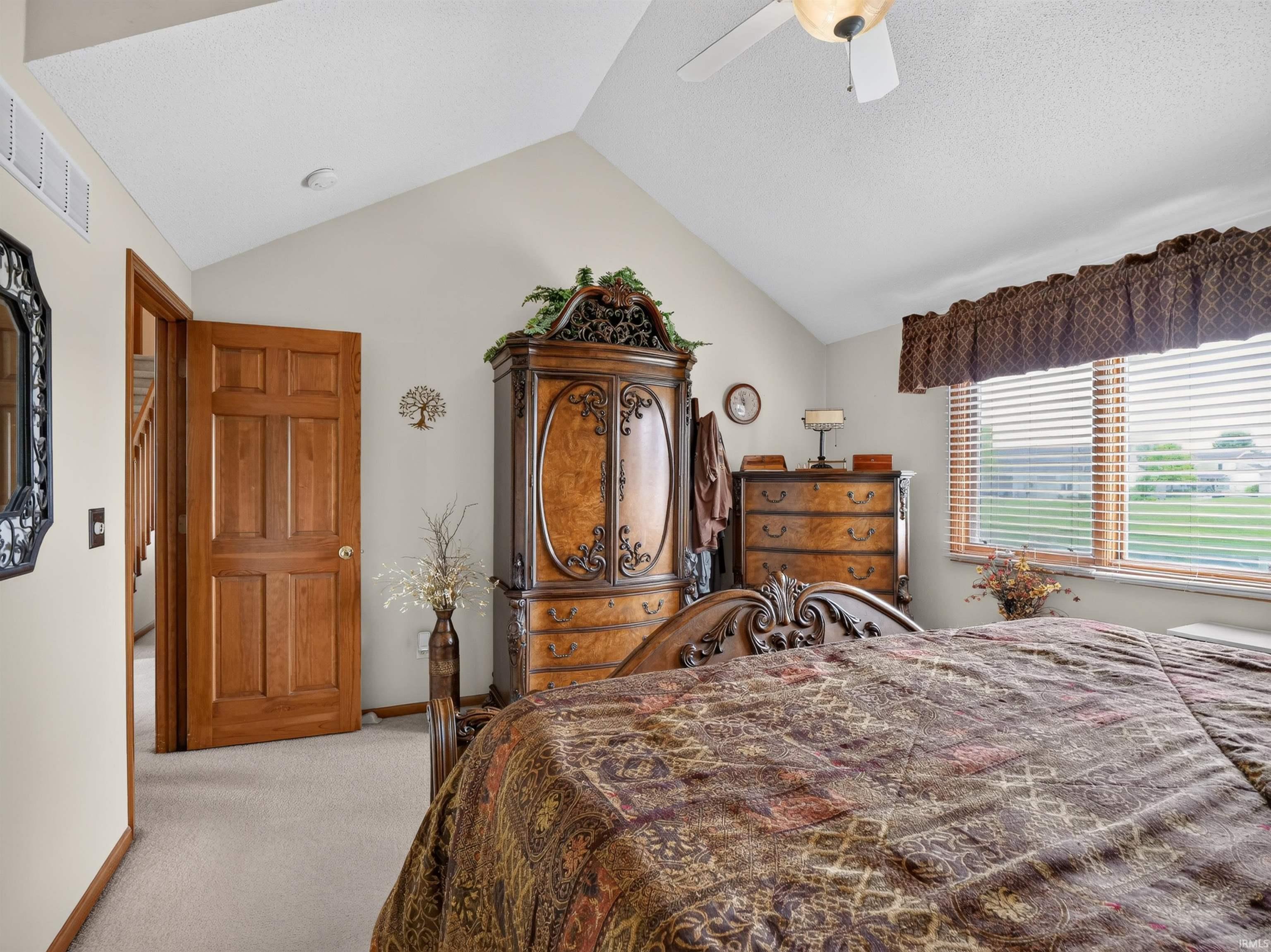 Vaulted ceiling bedroom featuring plush carpet flooring, a multi-pane window with blinds, and a paneled wooden door