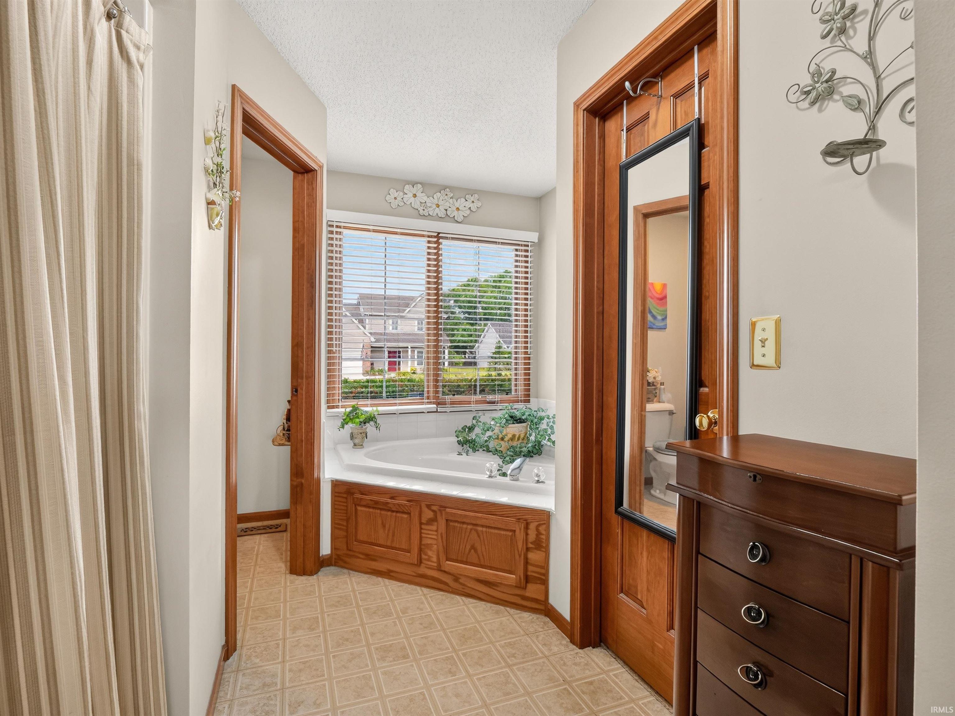 Soaking tub with a wood-panel surround and large window with blinds