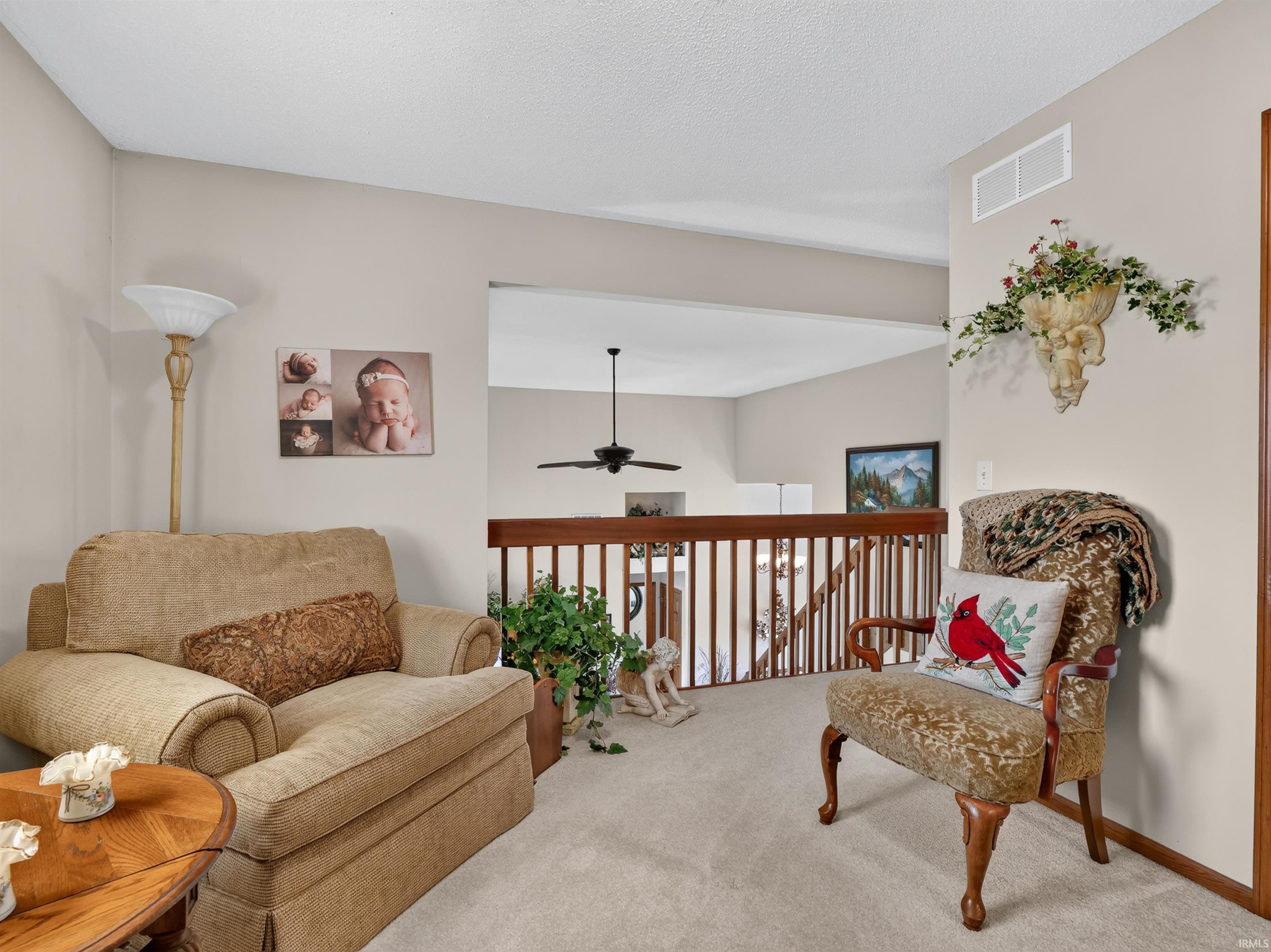 Carpeted common area featuring a wooden railing and a ceiling fan