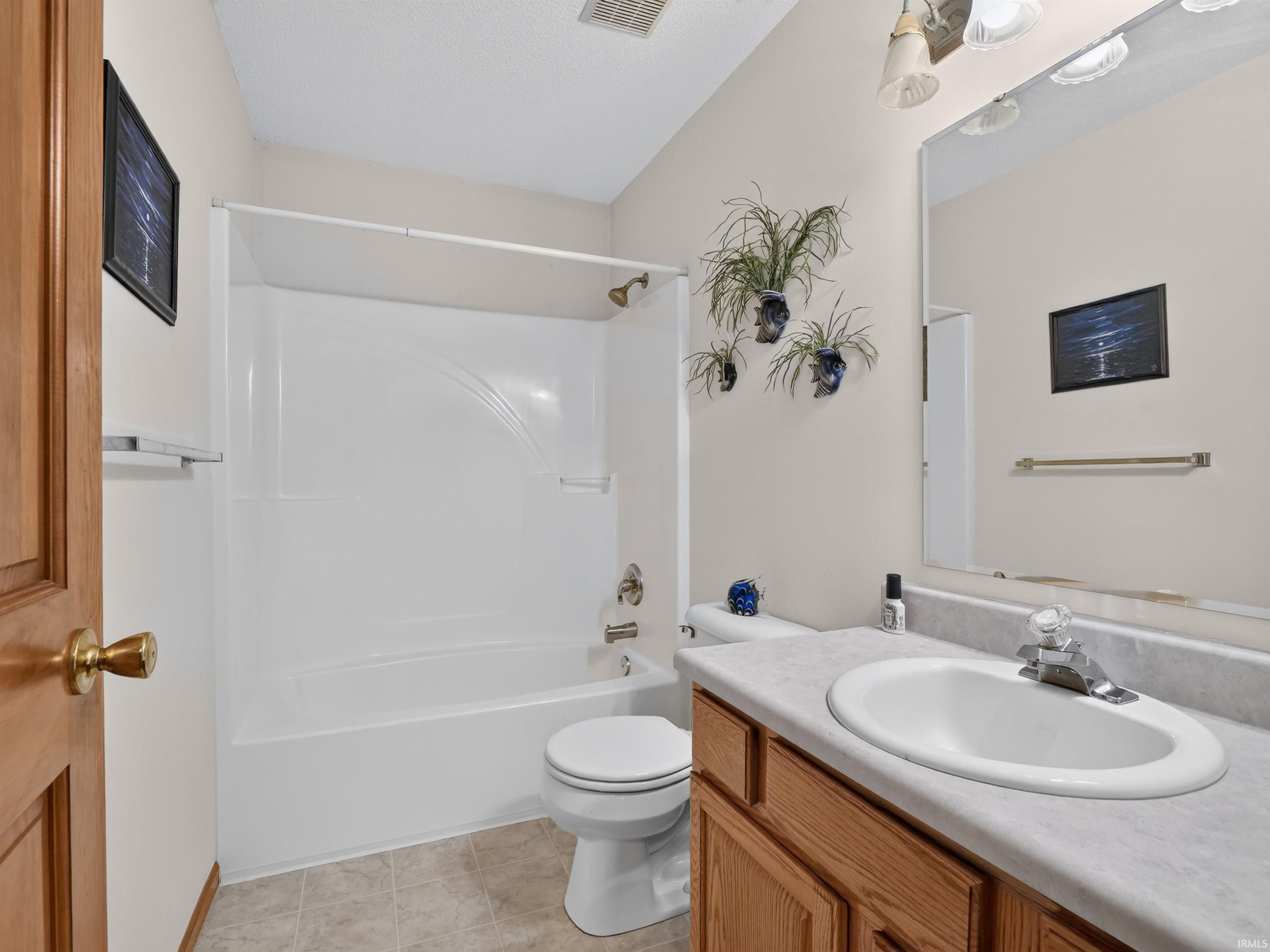 Bathroom featuring a white tub/shower combination, toilet, and a vanity with a laminate countertop and light wood-finish cabinetry