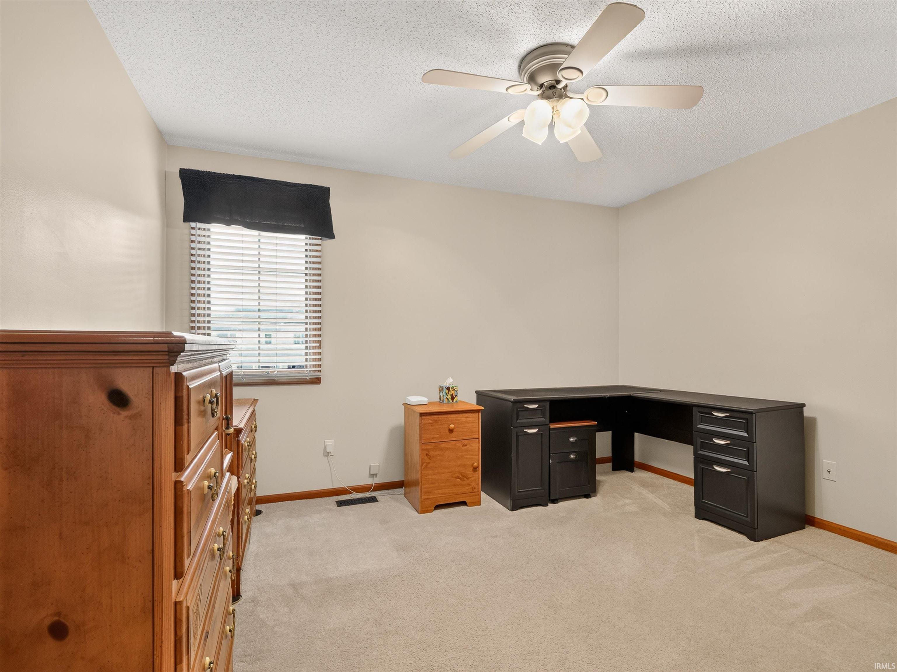 Carpeted room with a ceiling fan light fixture, neutral wall paint, and a window featuring blinds and a dark valance