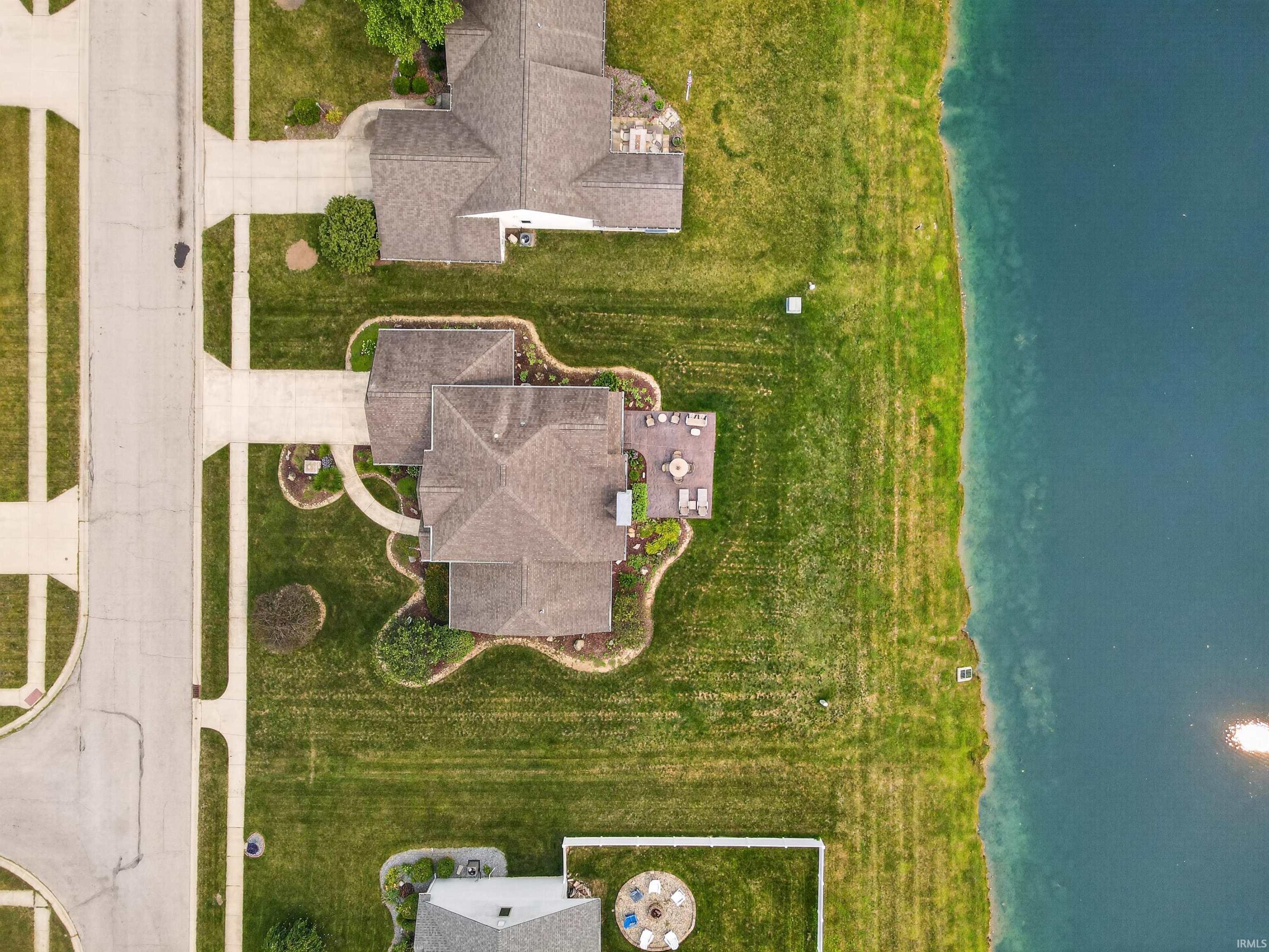 Aerial perspective highlighting the property's expansive green space, direct water frontage, and well-maintained hardscaping