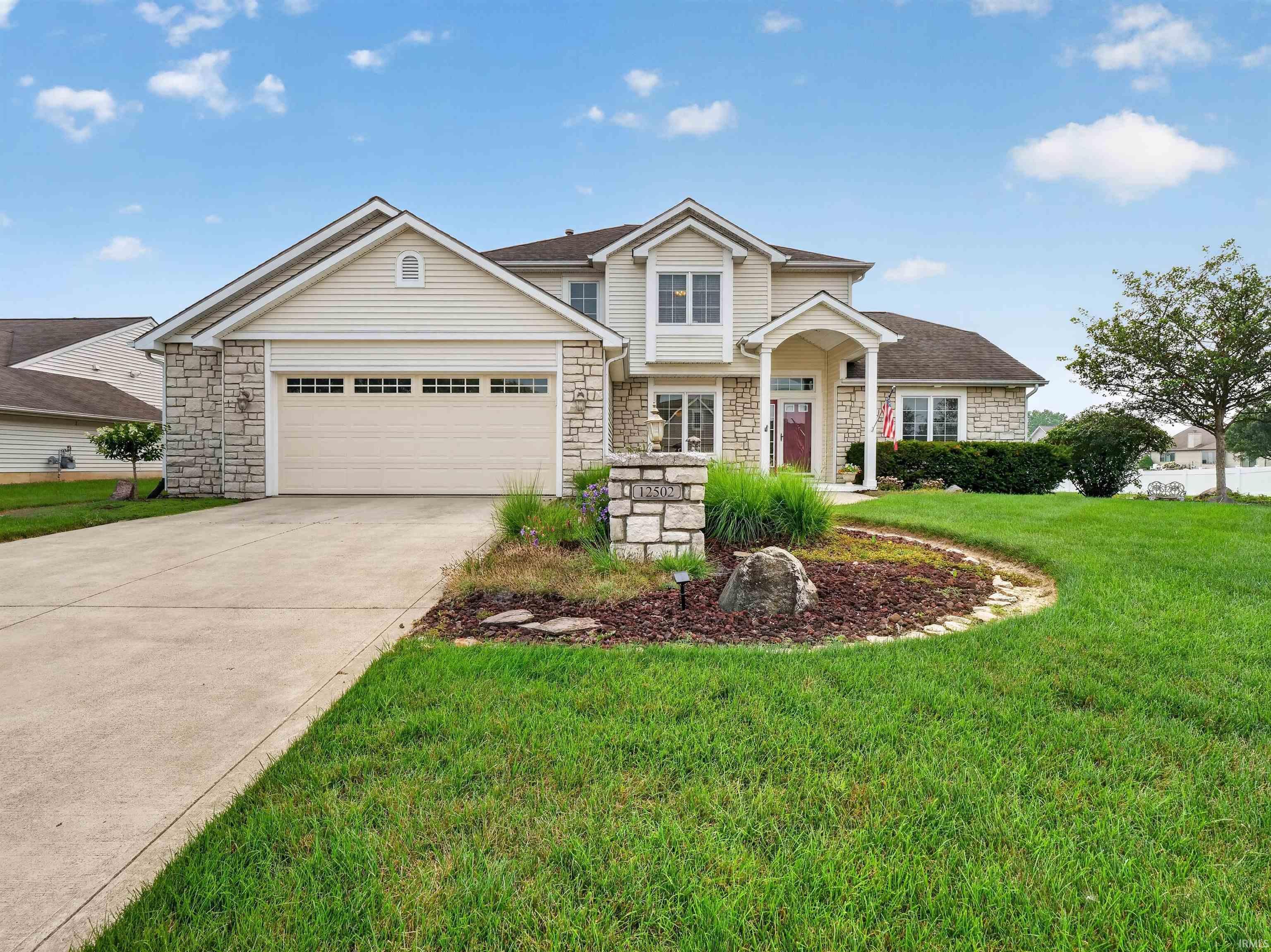 Stone and siding exterior featuring an arched entryway, attached garage, concrete driveway, and a landscaped front yard with a stone-clad mailbox pillar