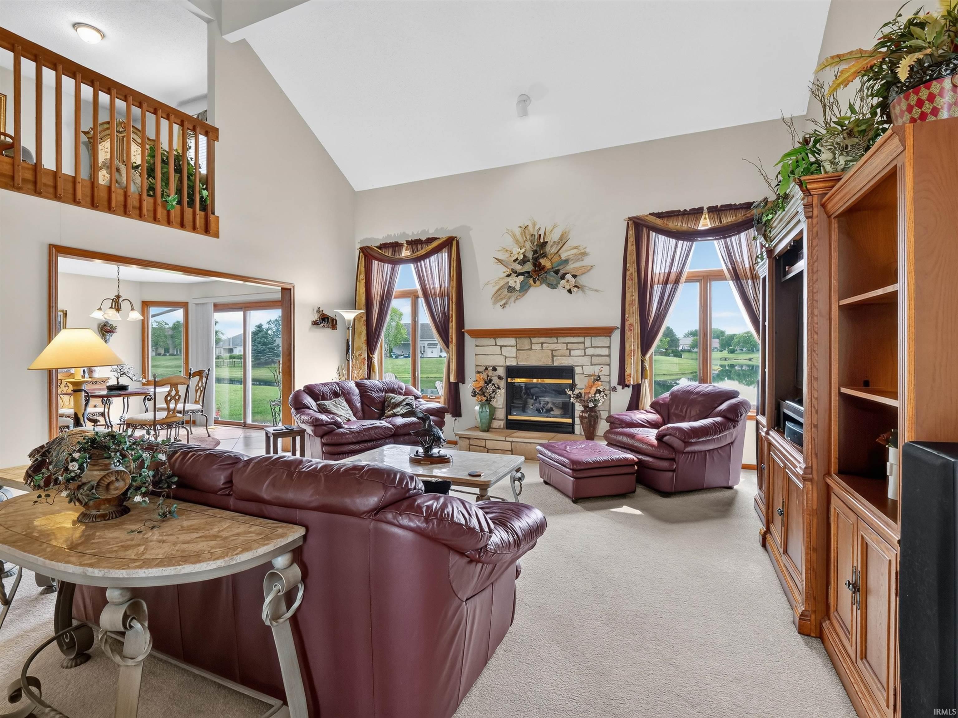 Vaulted ceiling living room featuring a stone fireplace, carpet flooring, a built-in entertainment center, and a balcony overlook