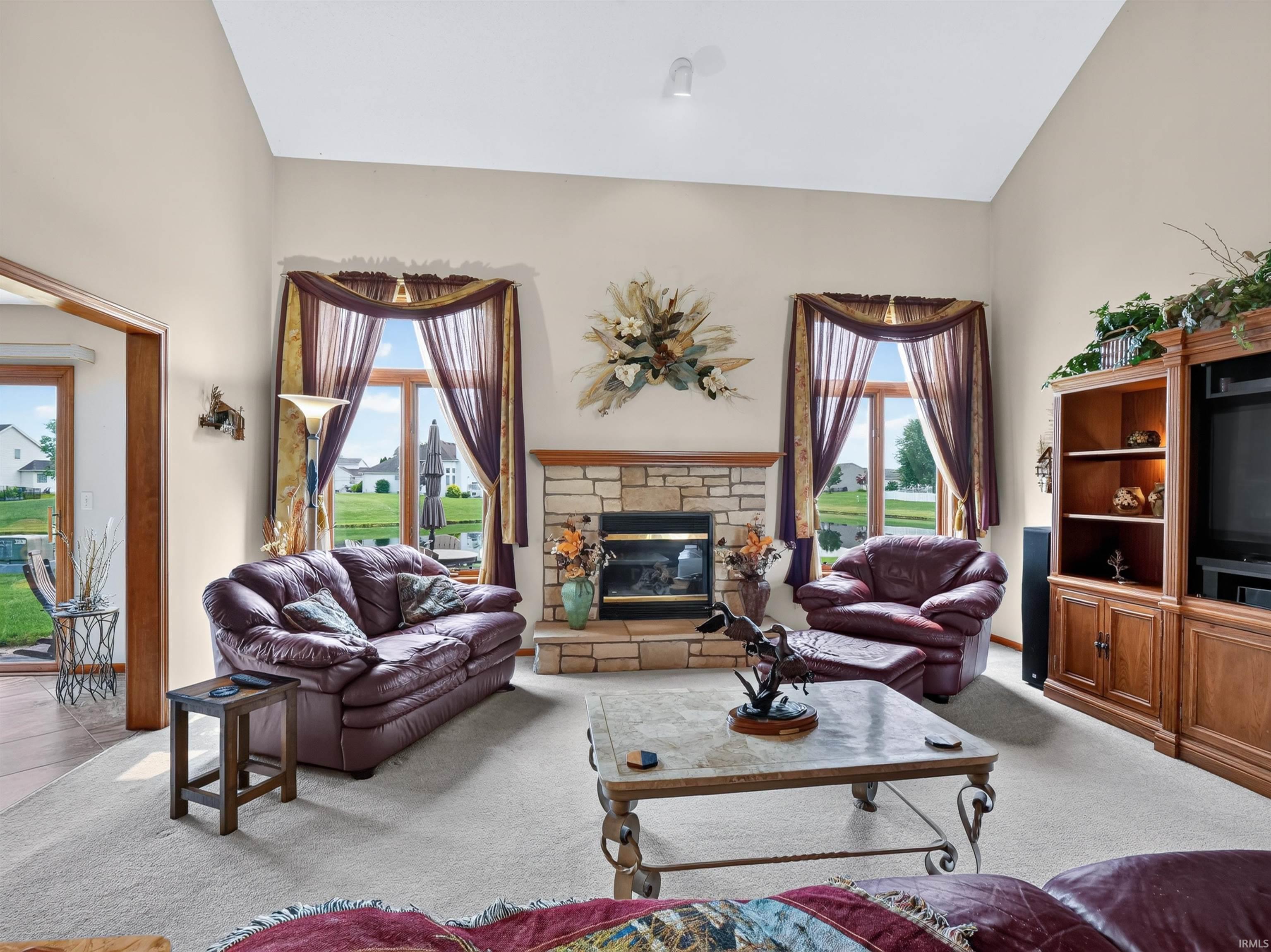 Spacious living area featuring a vaulted ceiling and a stone-faced fireplace with a wood mantel