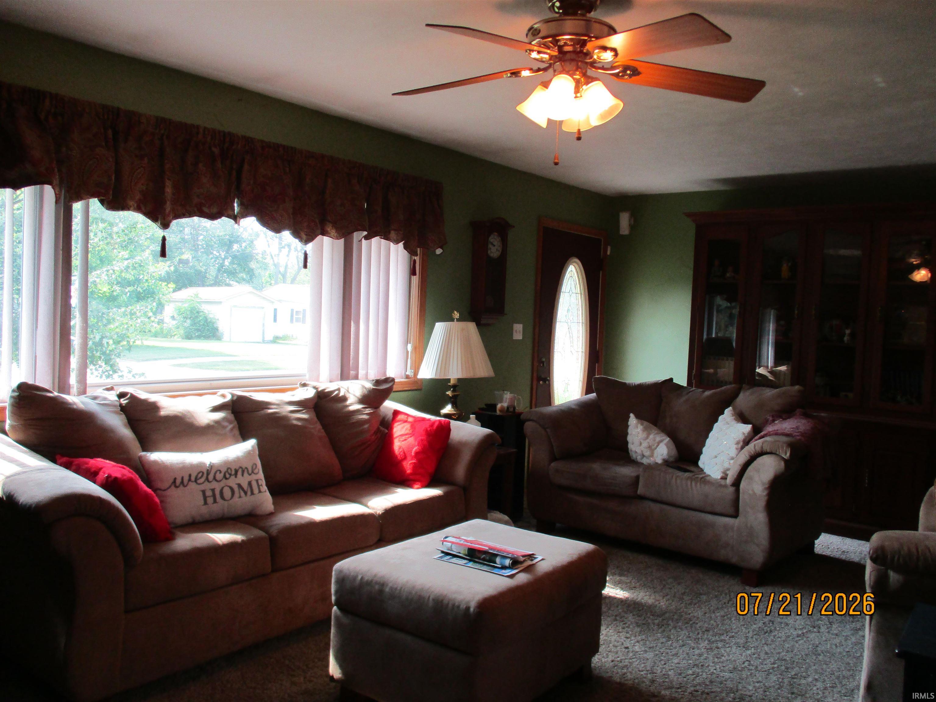 Bright living space featuring a ceiling fan with light fixture, large window with natural light, and a prominent entry door with an oval glass insert