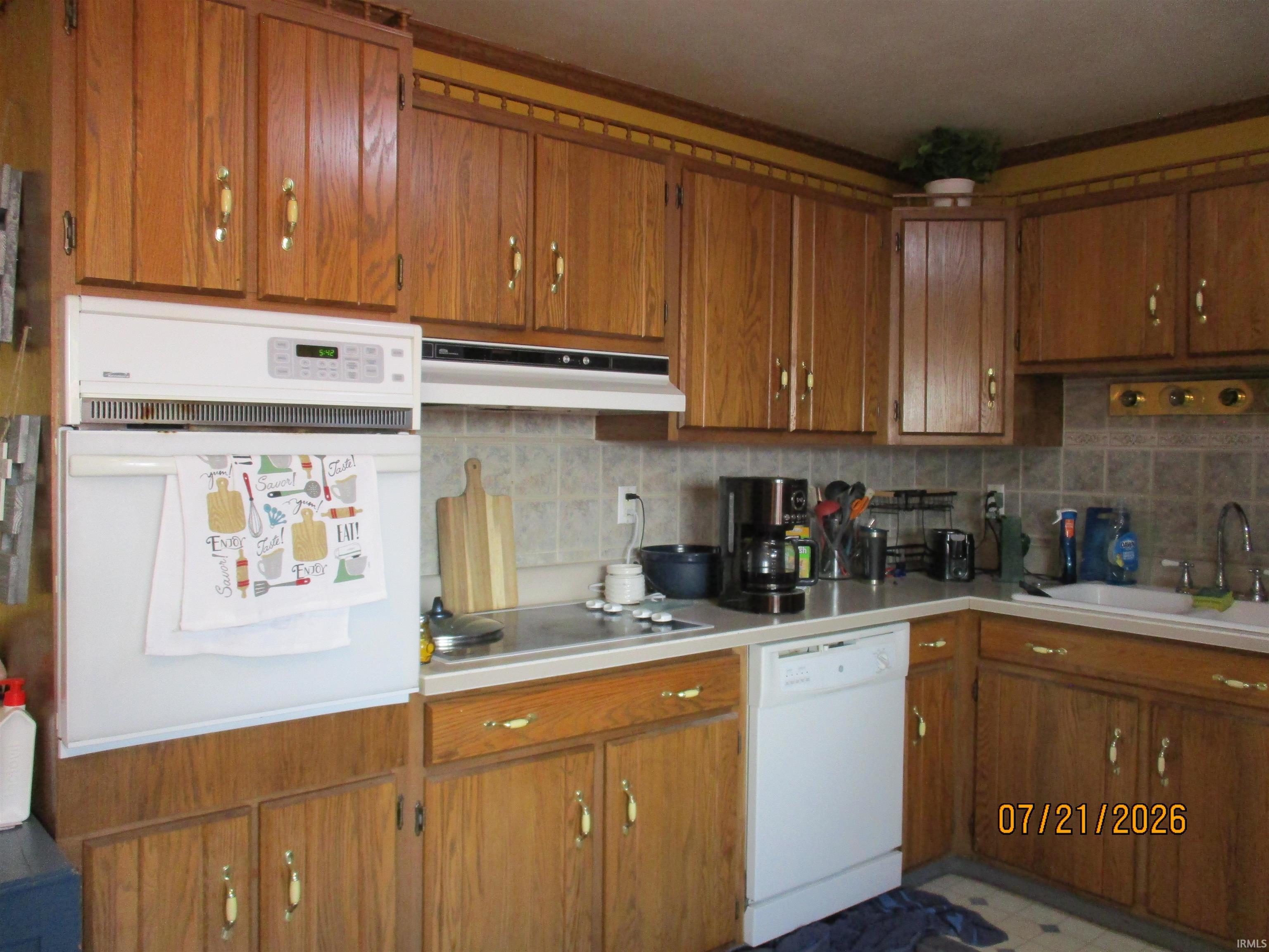 Kitchen featuring extensive wood cabinetry, an integrated wall oven, a white built-in dishwasher, and a double basin sink