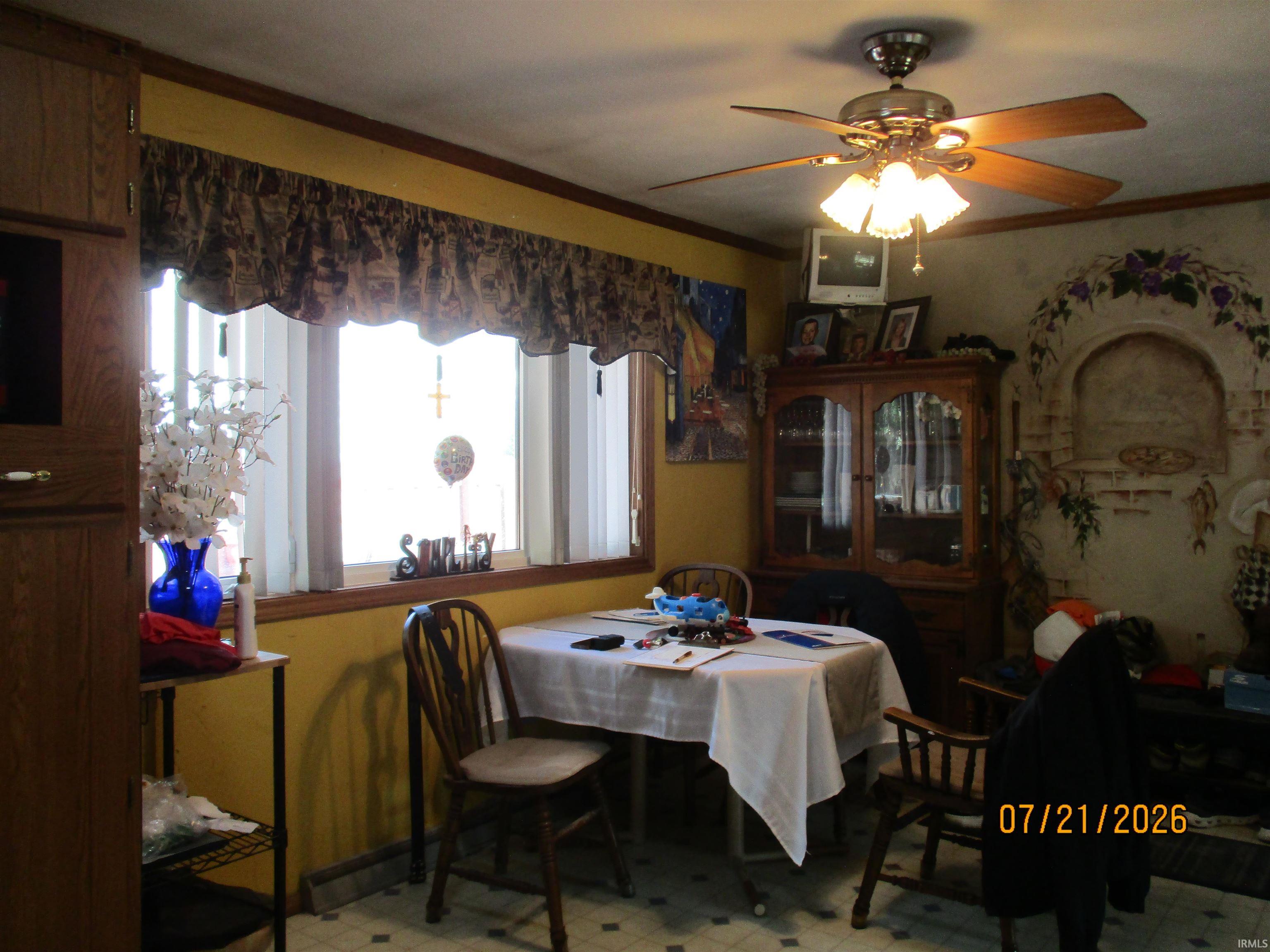 Bright dining space featuring a bay window, ceiling fan with integrated lighting, wood-finish cabinetry, and patterned floor tiling