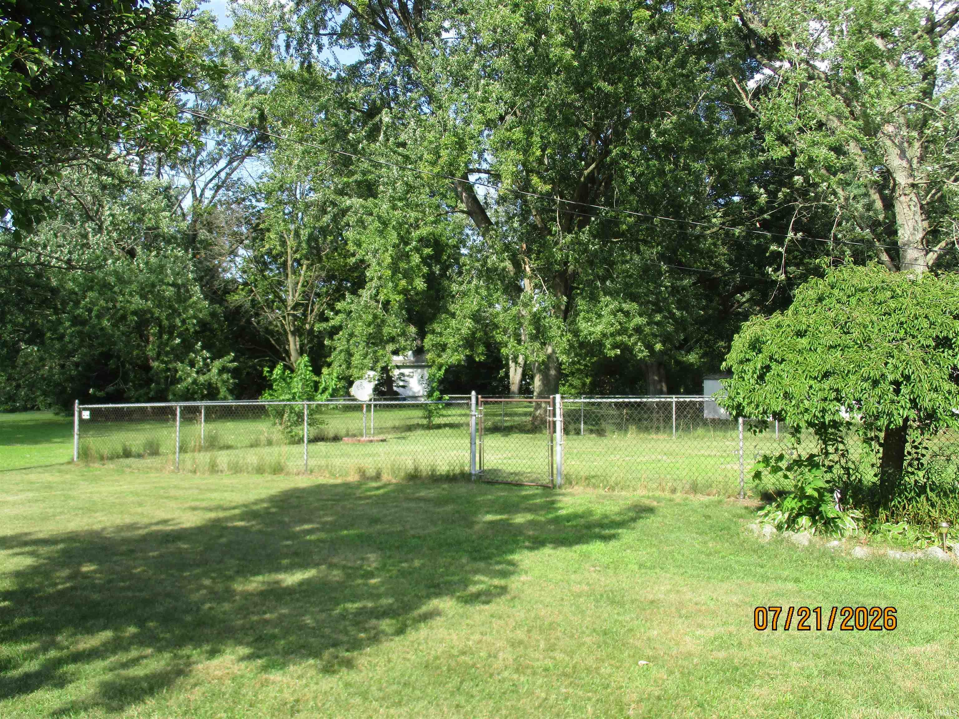 Expansive lawn area featuring a chain link fence and mature trees