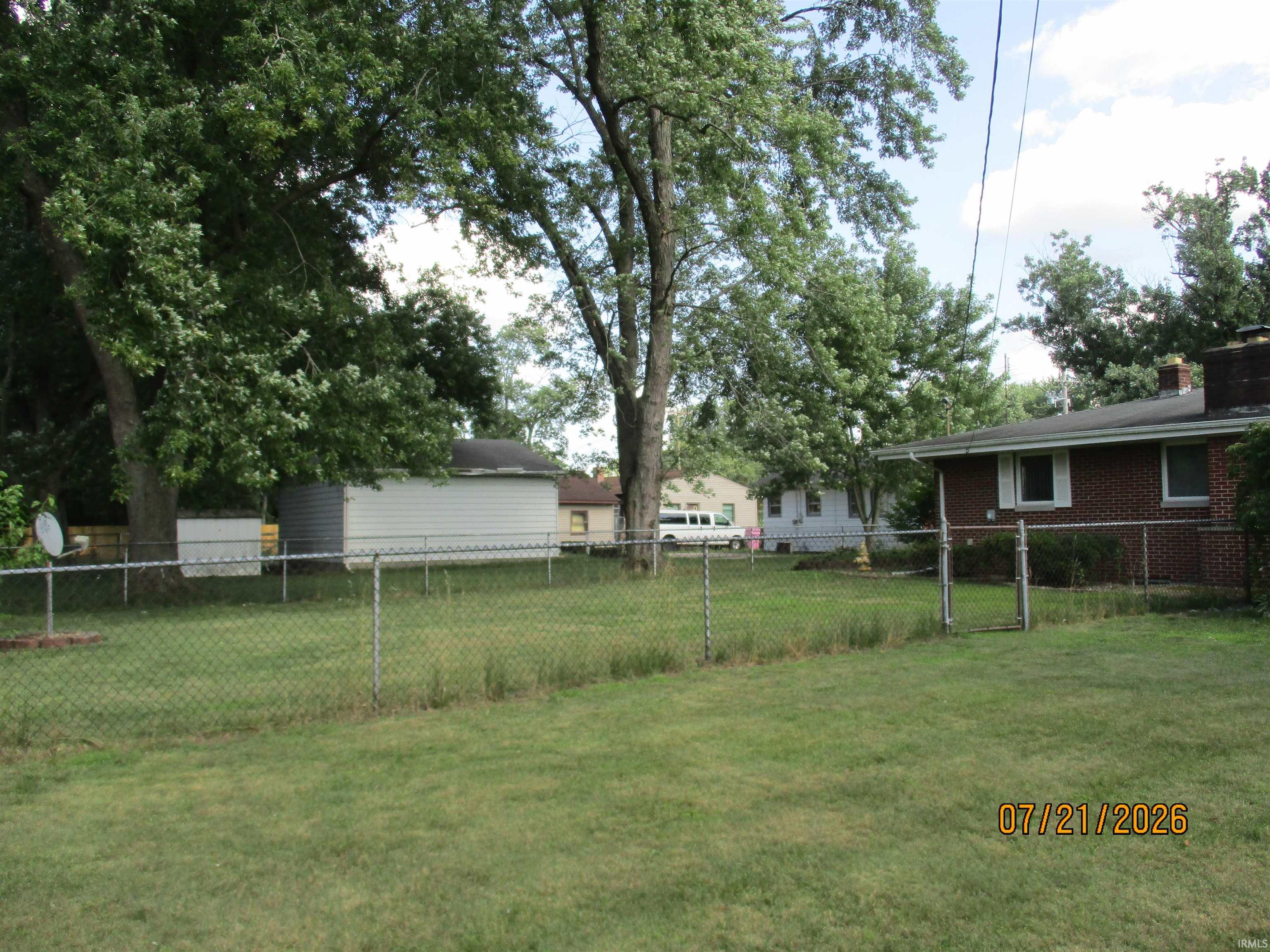Expansive grassy yard with chain-link fencing, mature trees, and a visible brick-clad structure