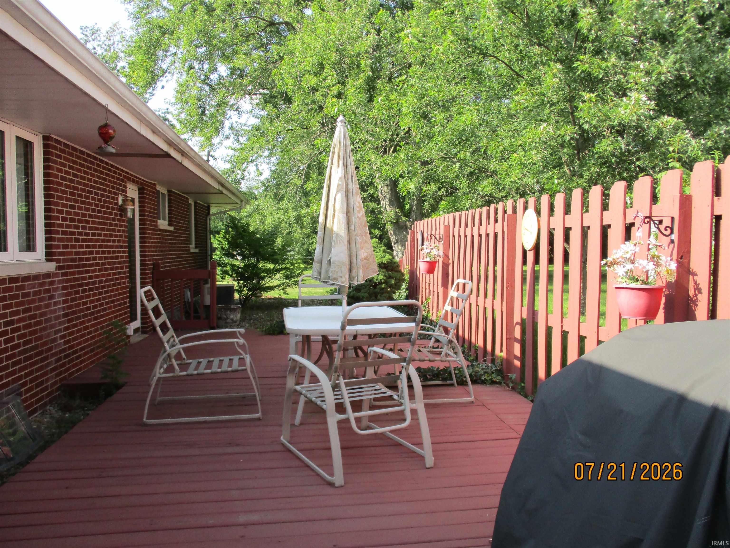 Red-stained wood deck featuring a red picket fence and mature perimeter foliage