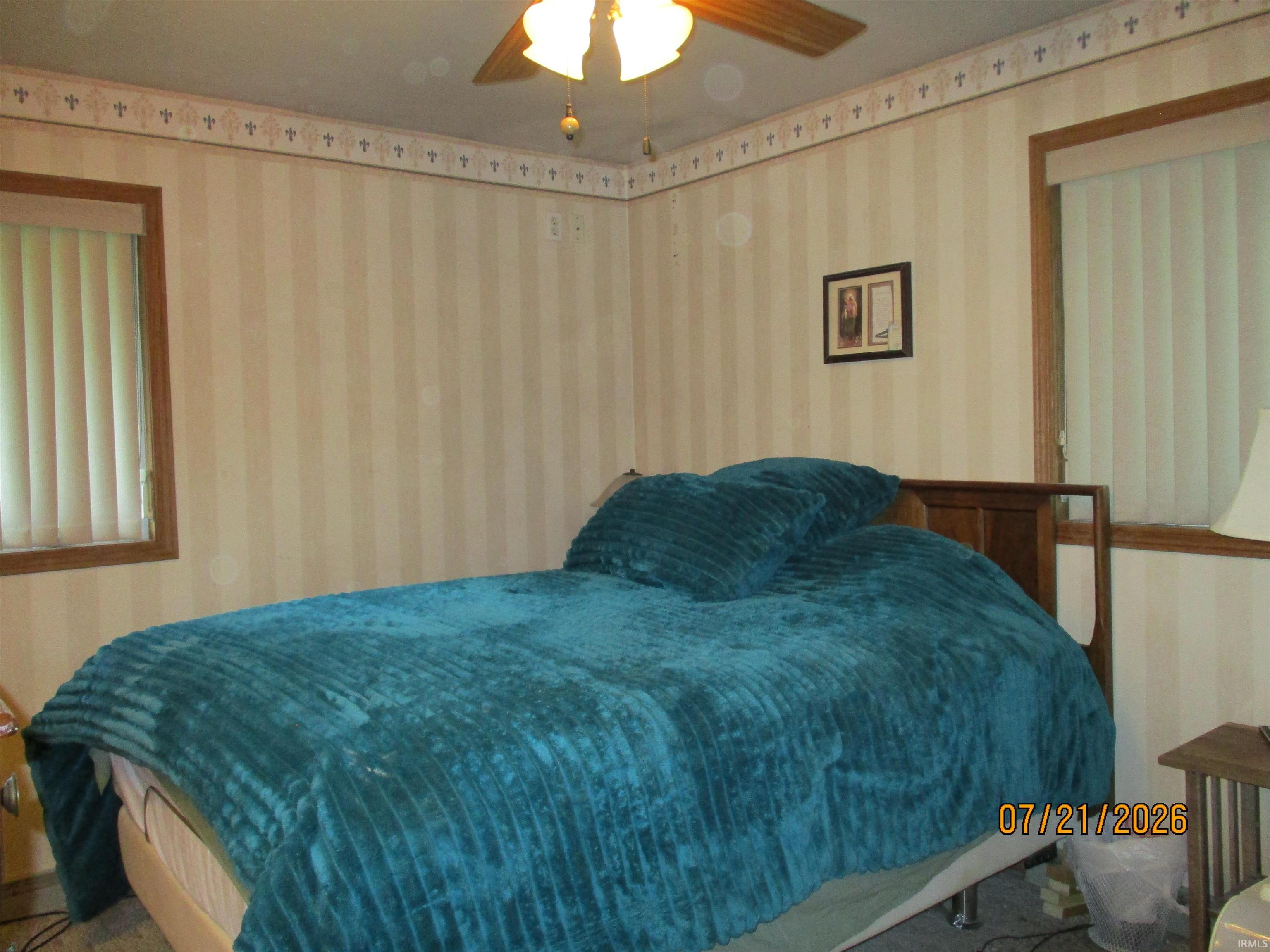 Room featuring striped wallpaper with a decorative border, two windows with vertical blinds and wood trim, and a ceiling fan with a light fixture