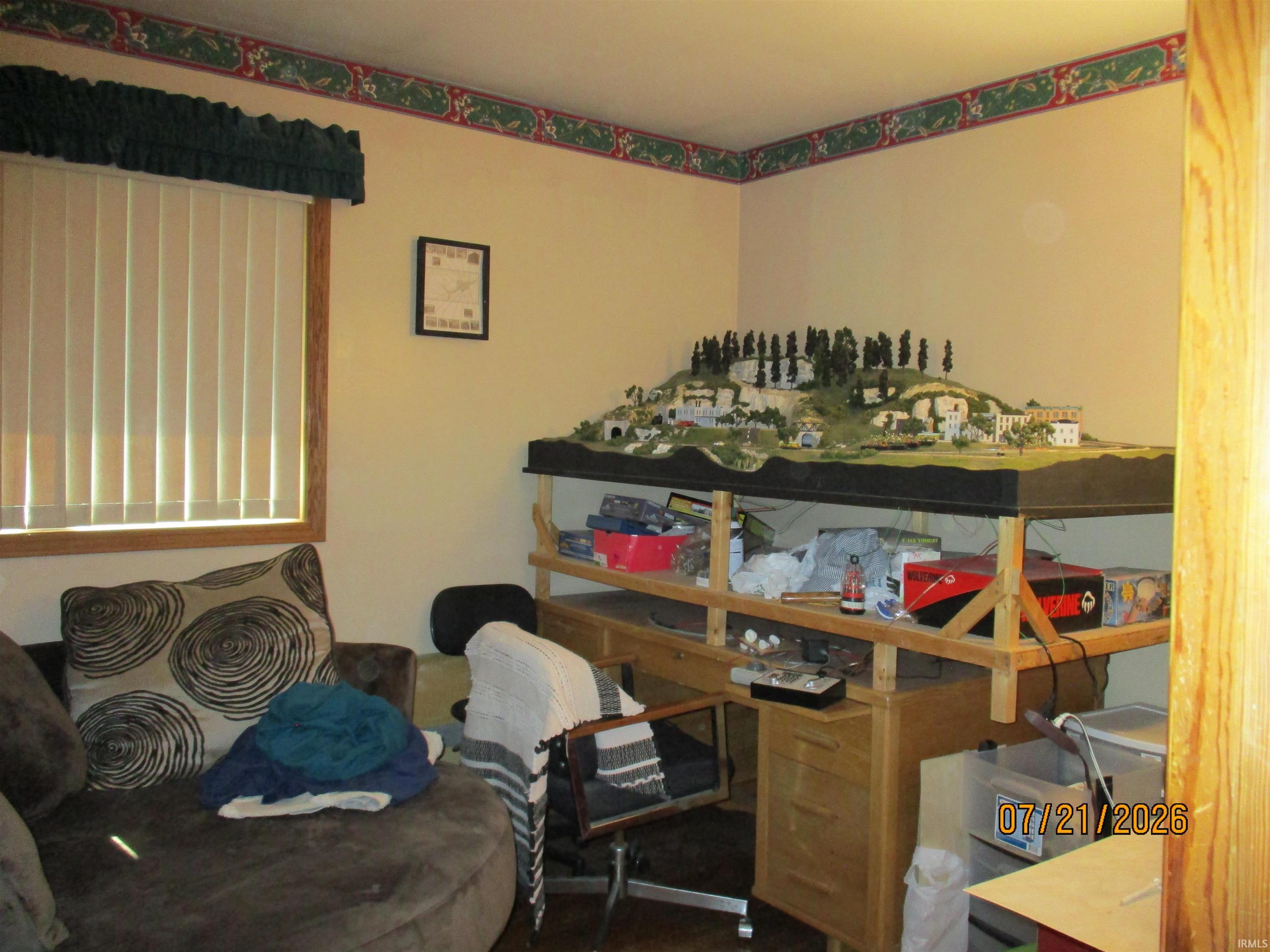 Room featuring a window with vertical blinds and a wood-finish frame, light beige walls, and decorative border trim