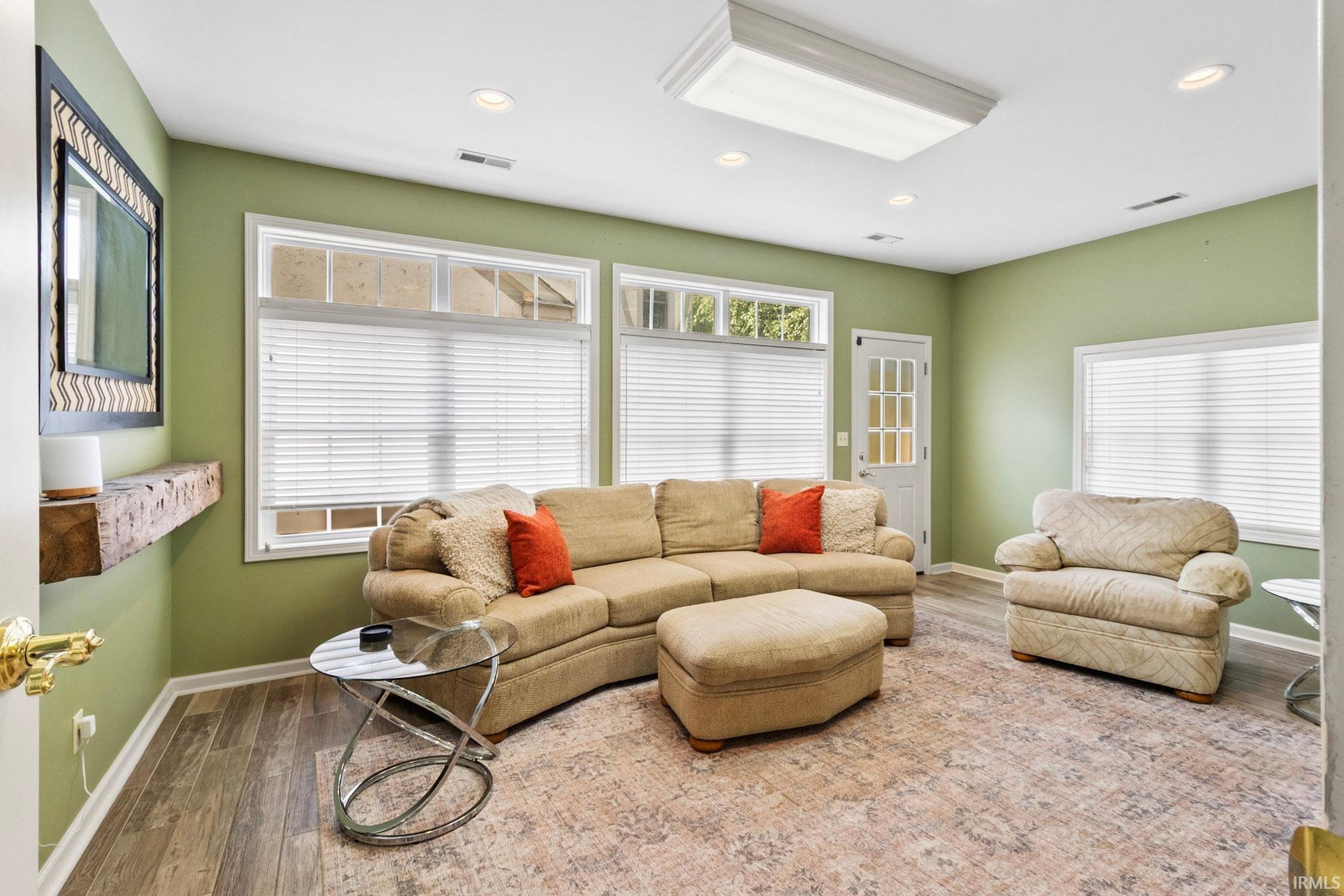 Spacious room featuring multiple windows with blinds, wood-finish flooring, recessed lighting, and a transom window above the exterior door