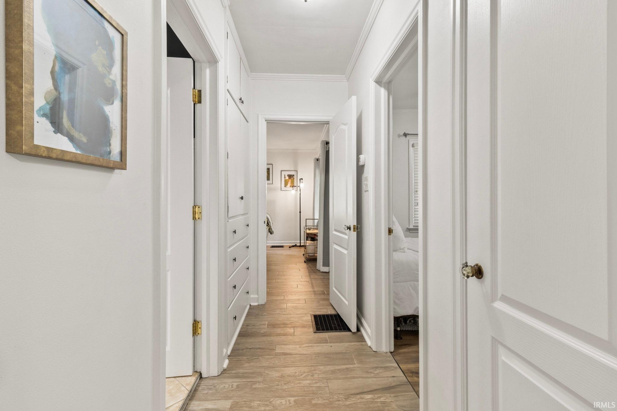 Hallway featuring wood-finish flooring, white paneled doors, and built-in cabinetry with drawers and brass hardware