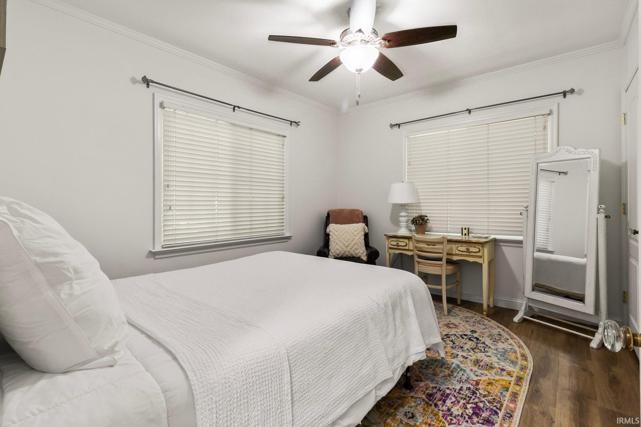 Bedroom featuring wood-finish flooring, two windows with blinds, a ceiling fan with integrated lighting, and crown molding