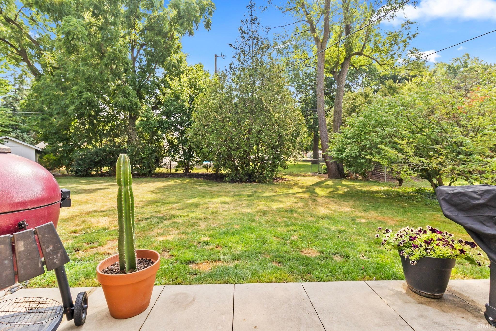 Spacious backyard featuring a manicured lawn, established trees, and a concrete patio