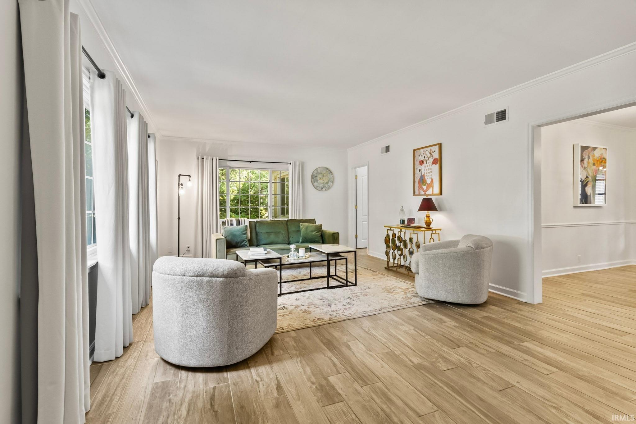 Bright living space featuring wood-finish flooring, multiple windows, white crown molding, and an open doorway to an adjoining room