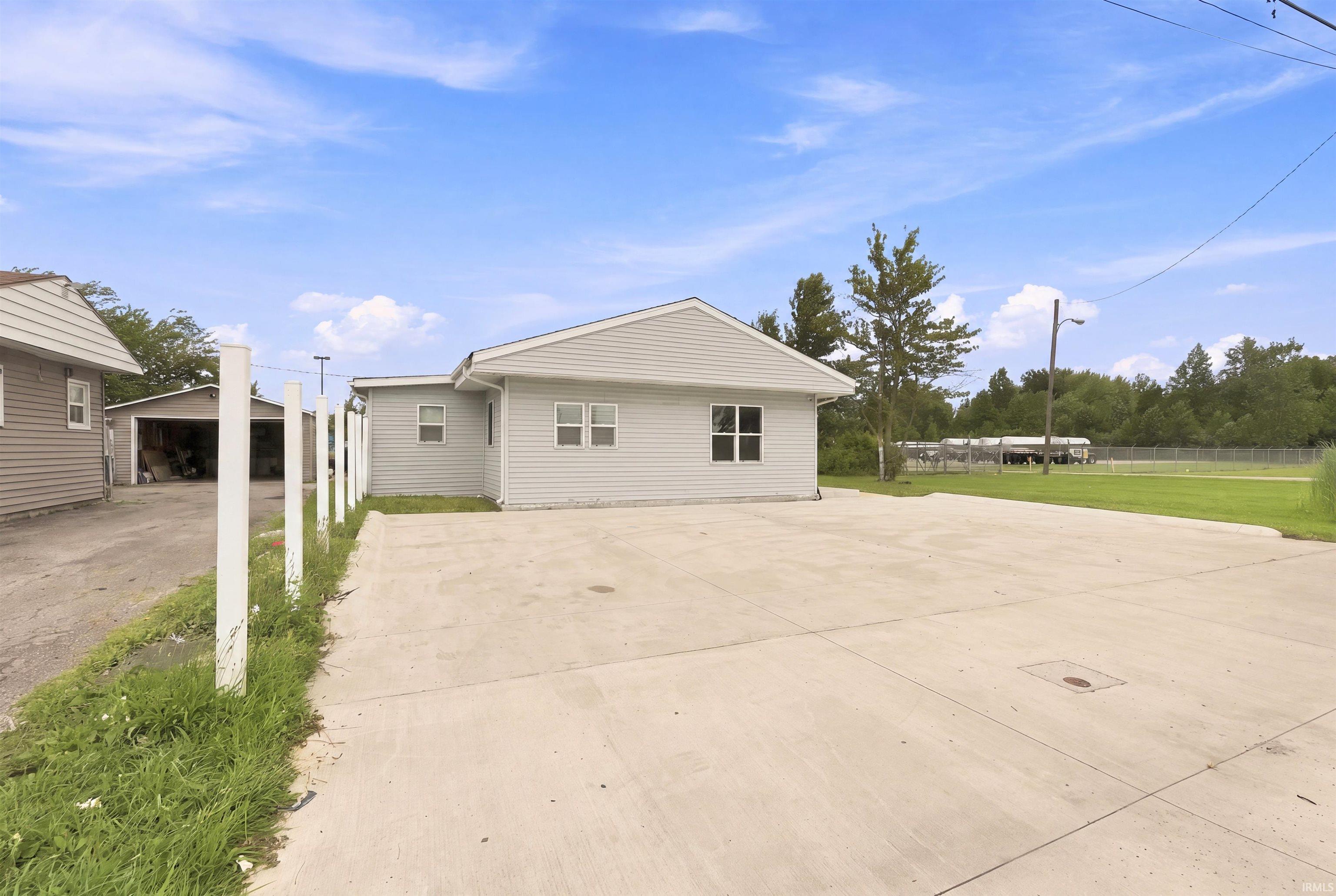 Light-colored siding exterior with a concrete parking area and a separate garage structure