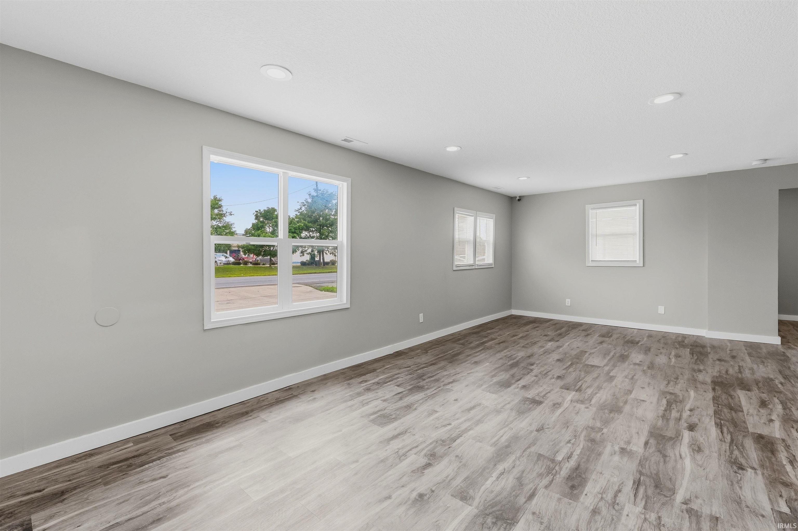 Spacious room featuring wood-finish flooring, recessed ceiling lighting, light gray wall paint, and multiple windows with white trim