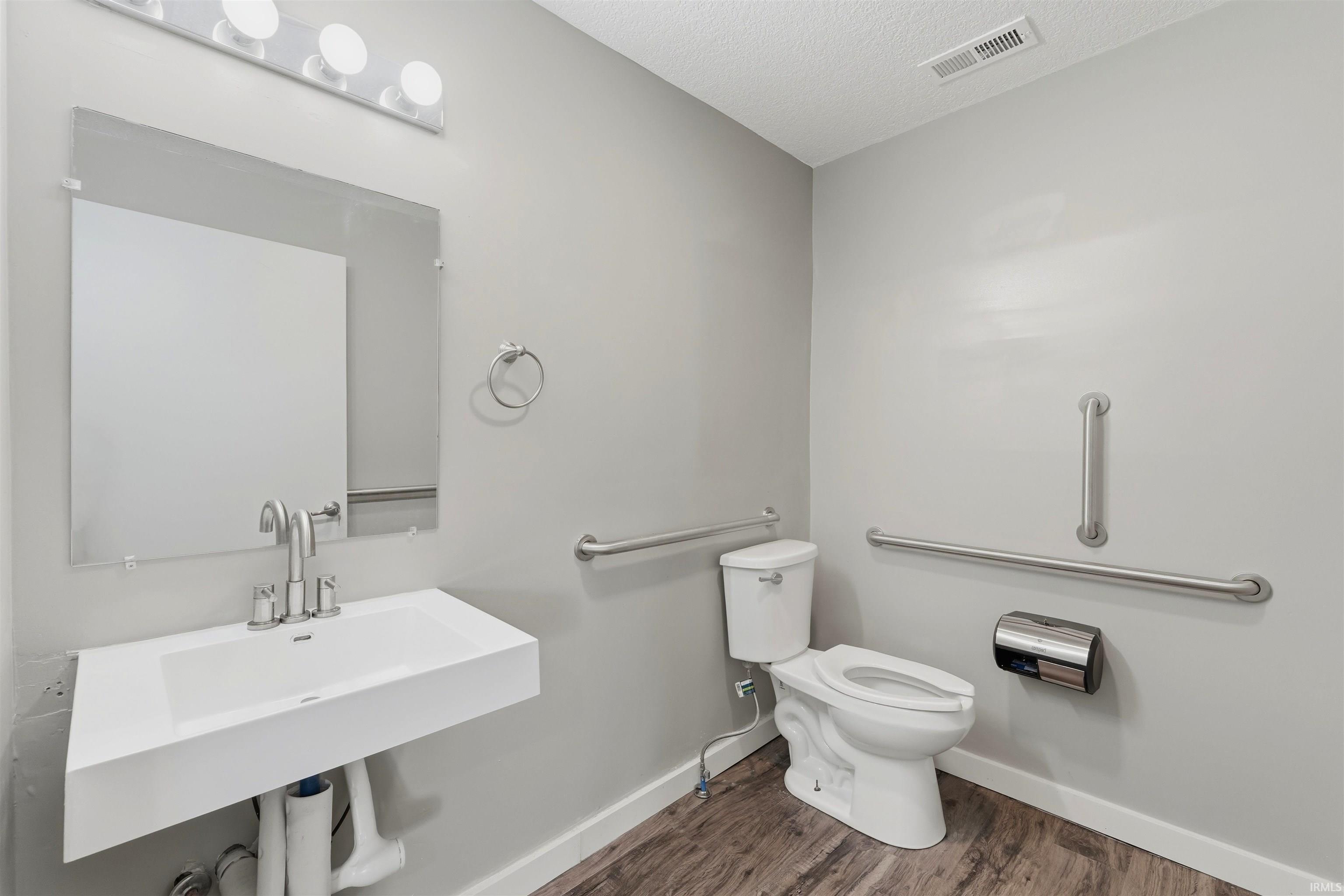 Bathroom featuring a wall-mounted sink, rectangular frameless mirror, and wood-finish flooring