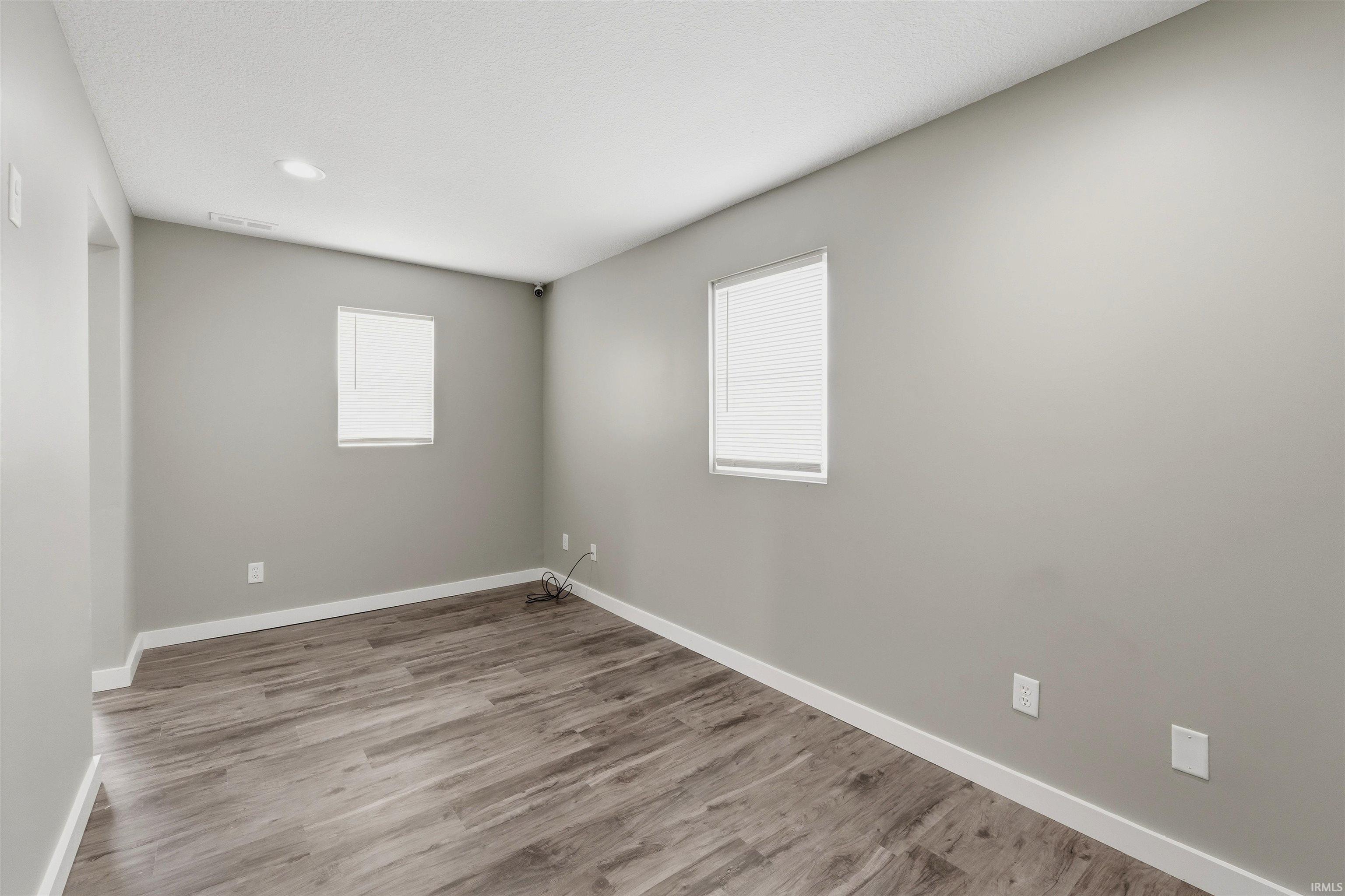 Spacious room featuring wood-finish flooring, two windows with blinds, recessed ceiling lighting, and light gray wall paint