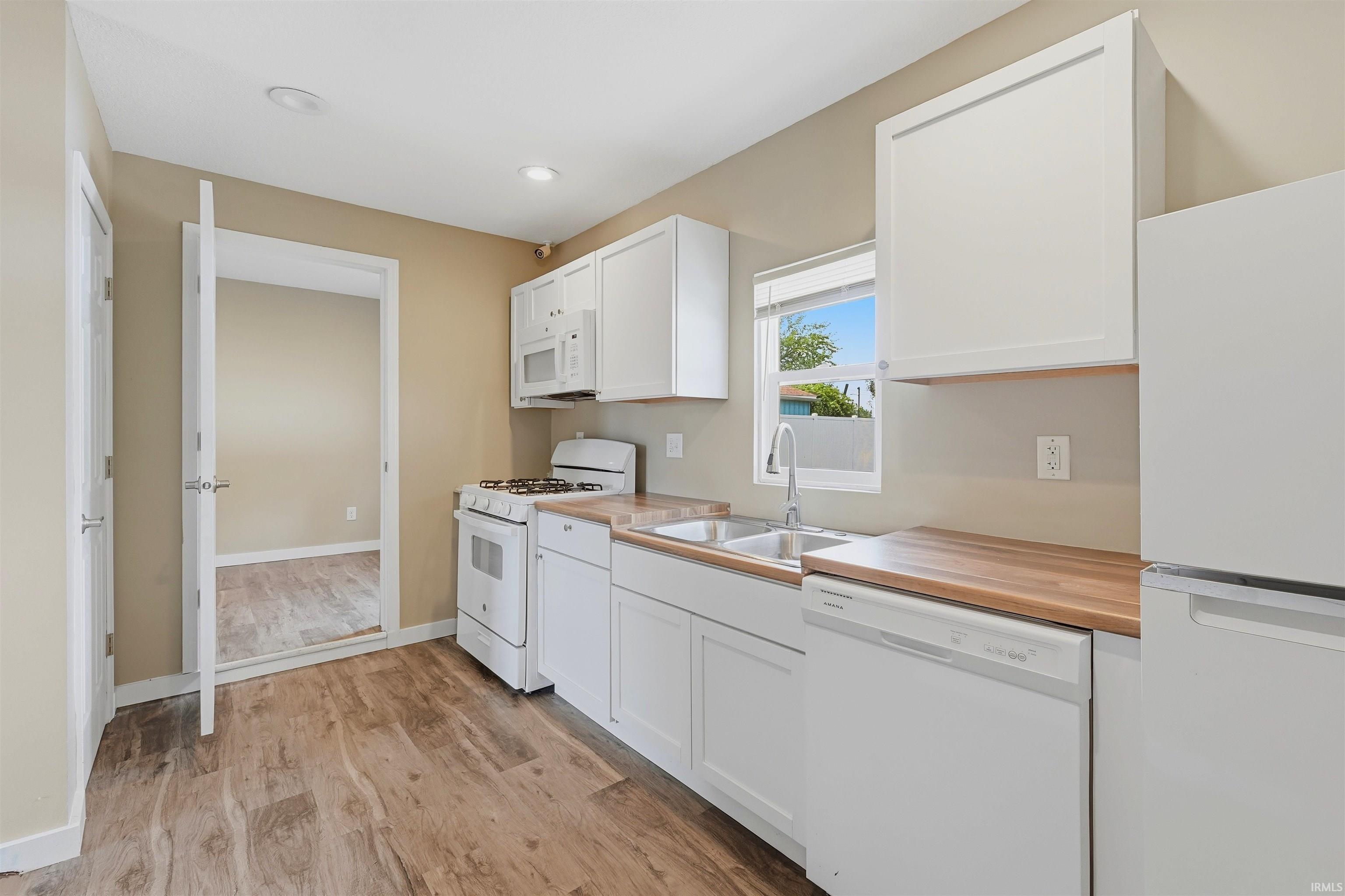 Kitchen featuring white cabinetry, wood-finish countertops, stainless steel sink, and wood-finish flooring