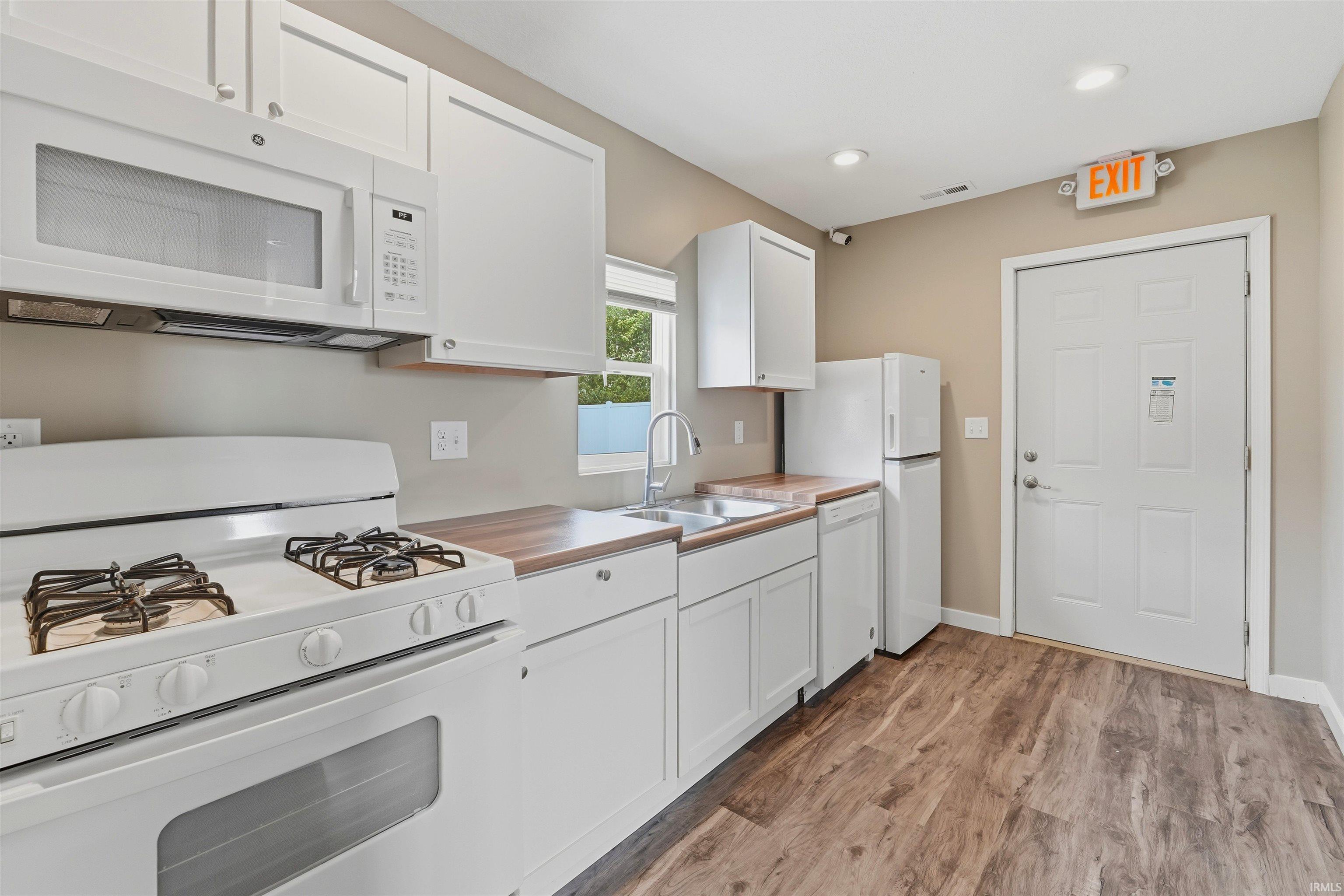 Kitchen featuring white cabinetry, wood-finish countertops, stainless steel sink, and wood-finish flooring