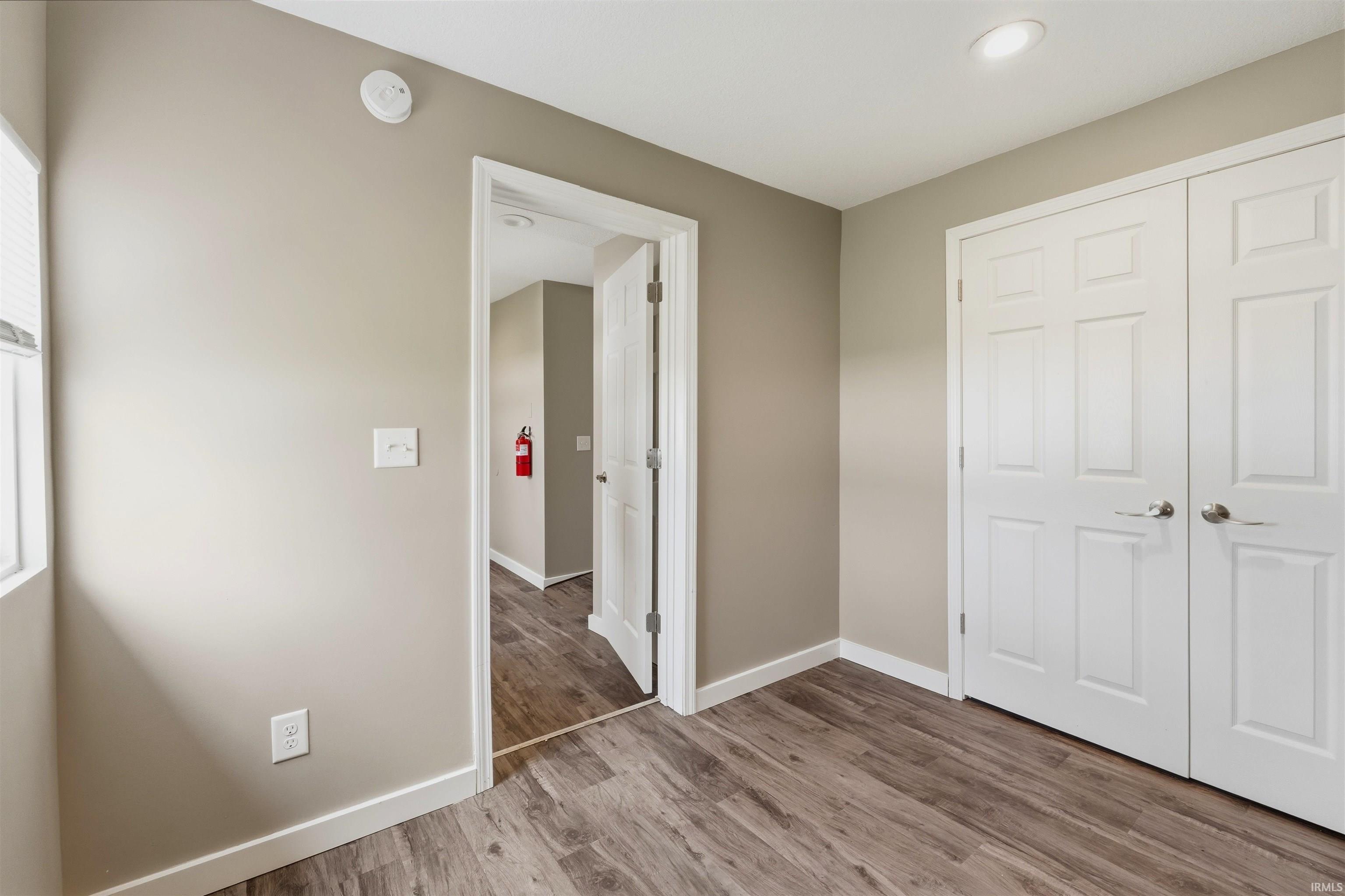 Room featuring wood-finish flooring, two-panel interior doors, recessed ceiling lighting, and a window with horizontal blinds