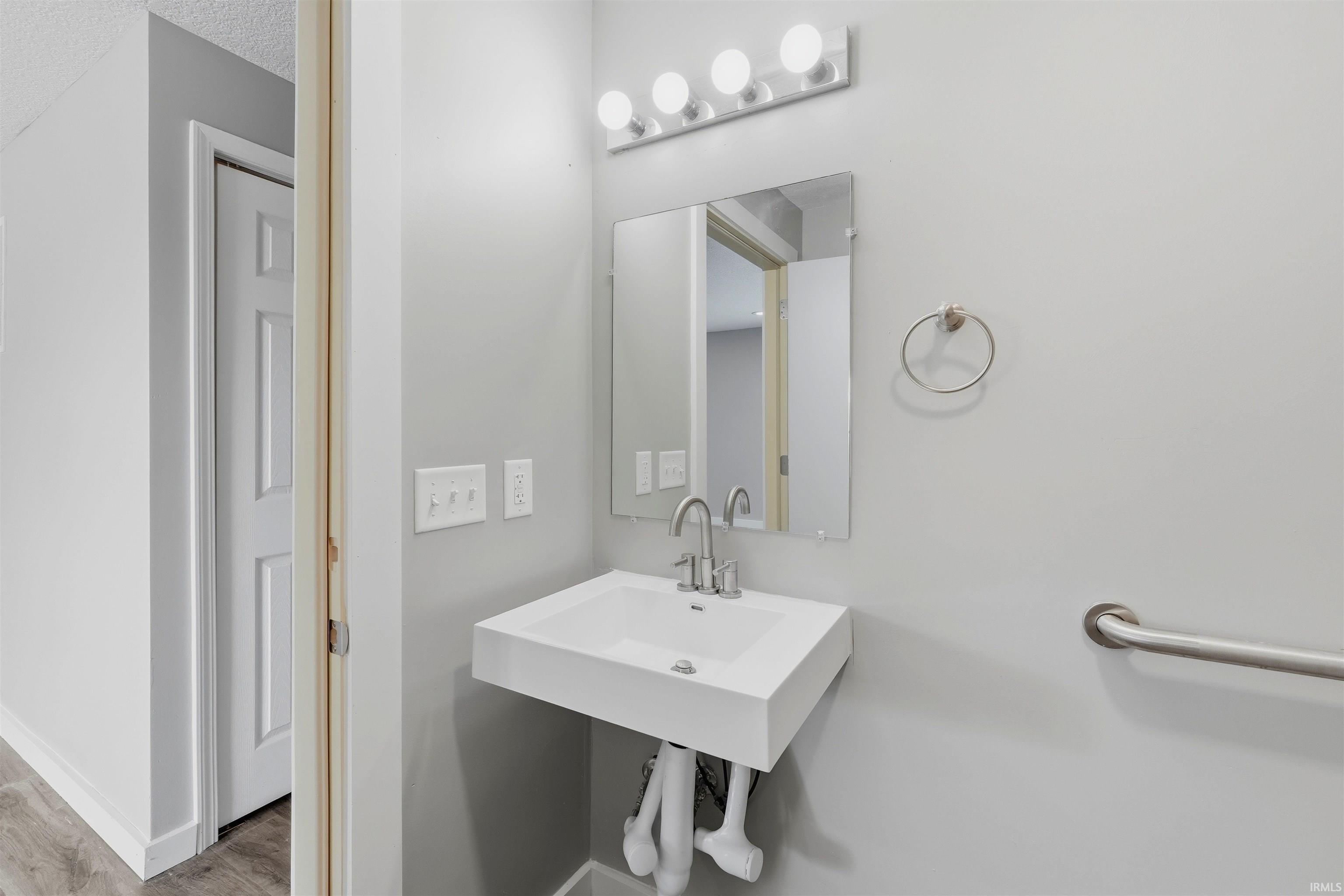 Wall-mounted sink with a chrome faucet, rectangular mirror, and a four-bulb vanity light fixture