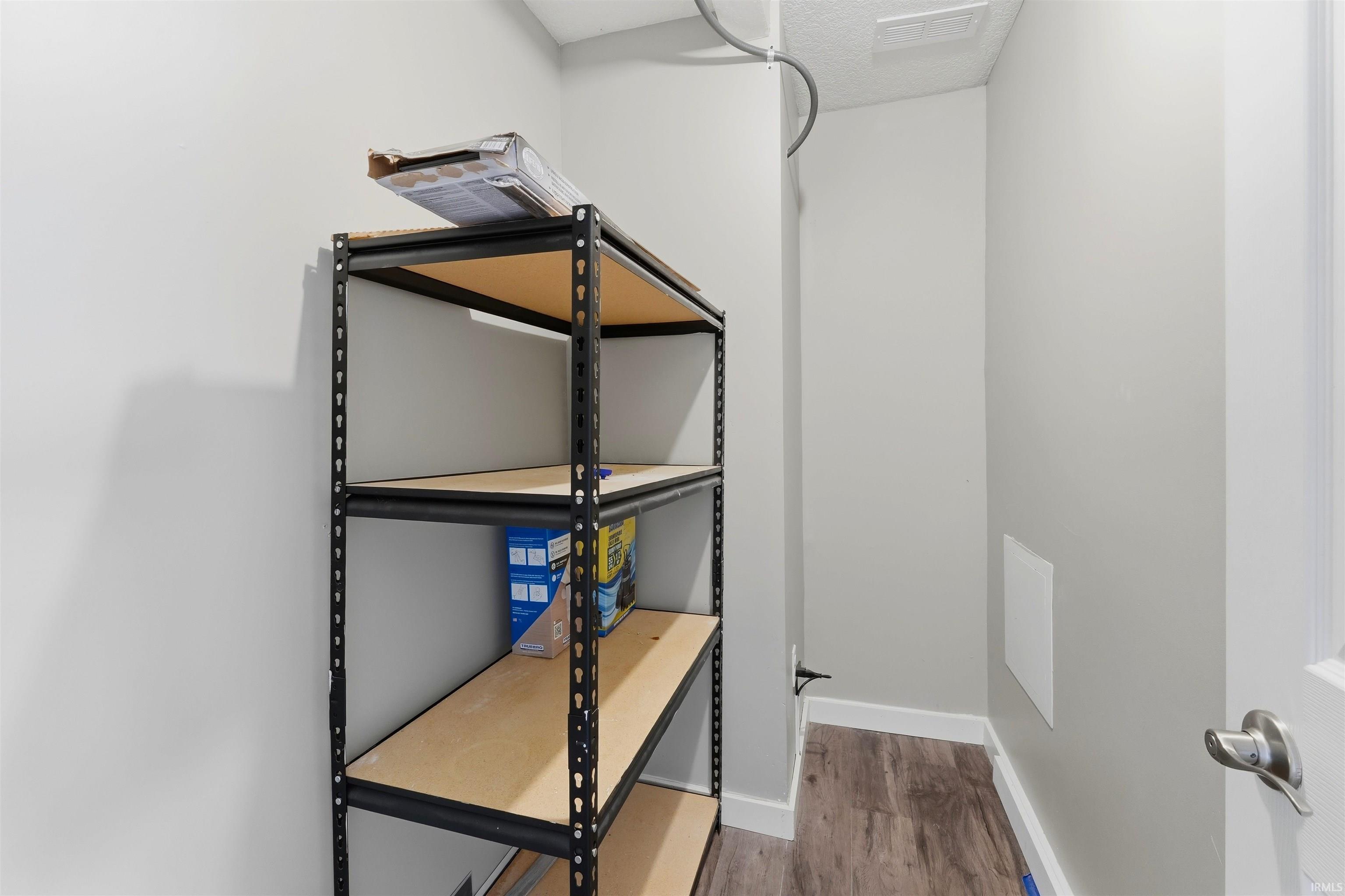 Utility room featuring wood-finish flooring, light grey walls, white baseboards, and a white door with a satin nickel handle