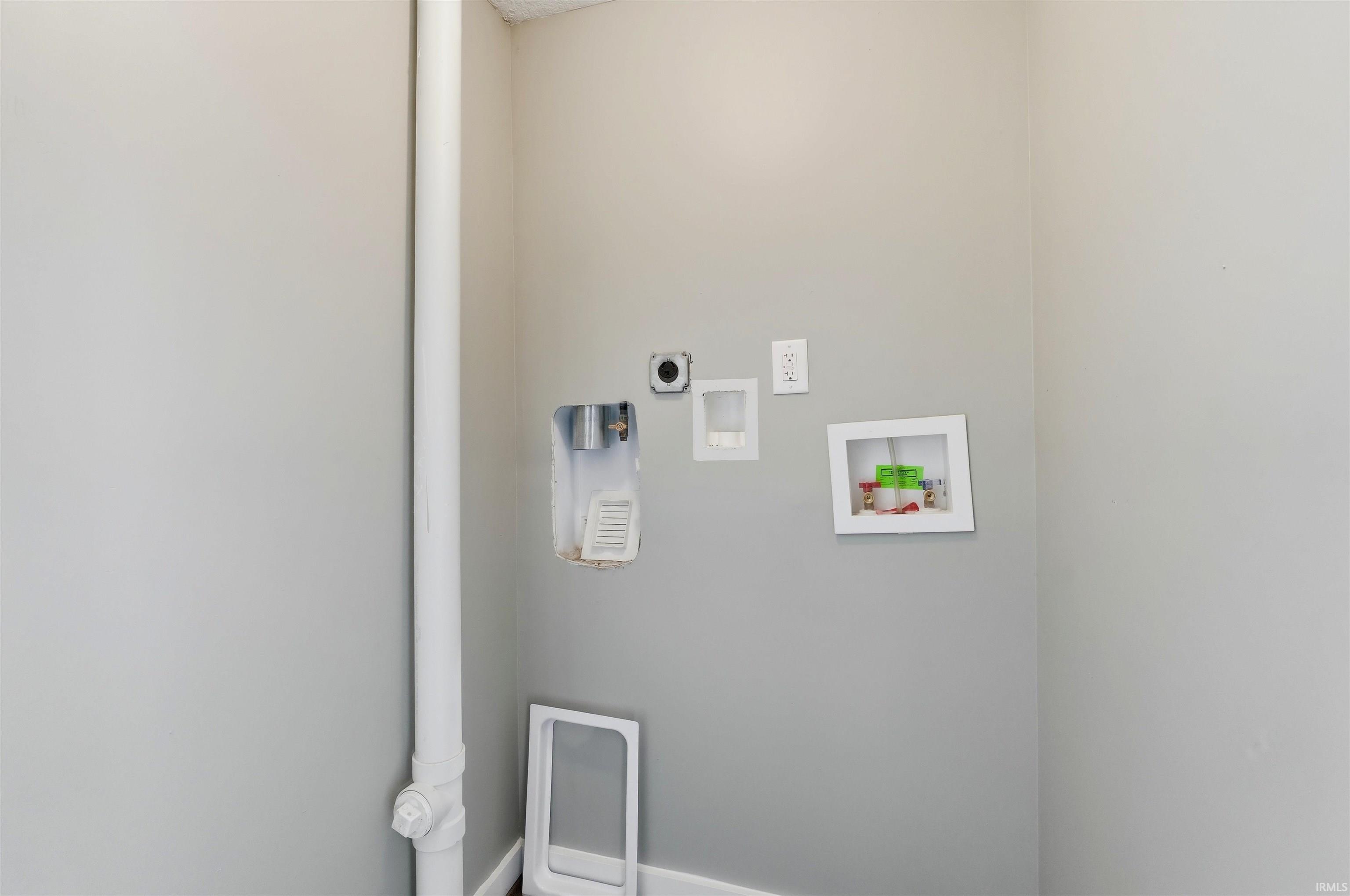 Utility area with light gray wall paint, wall-mounted electrical outlet, and plumbing hookups