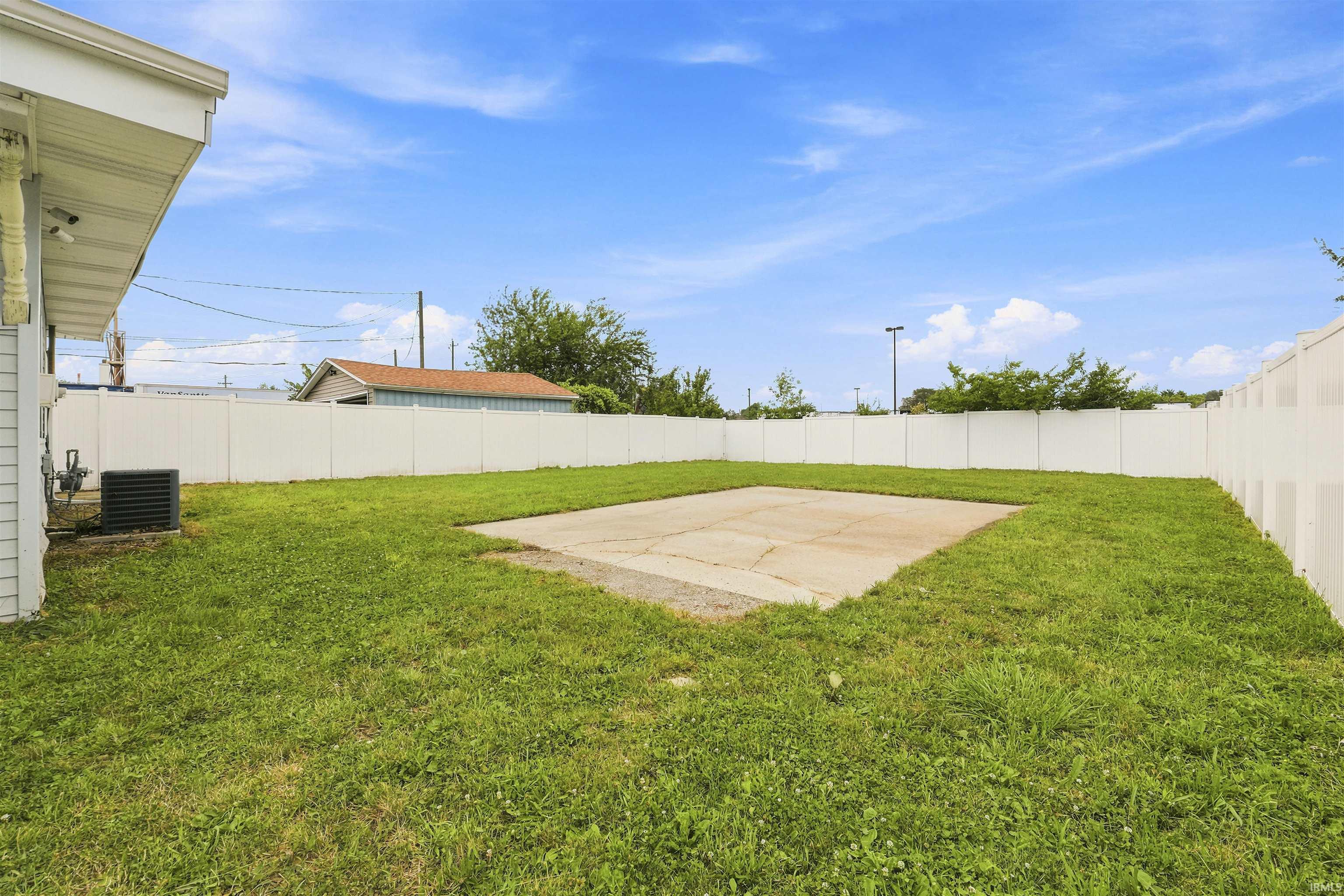 Expansive backyard featuring a concrete patio slab, surrounded by green lawn and a full privacy fence