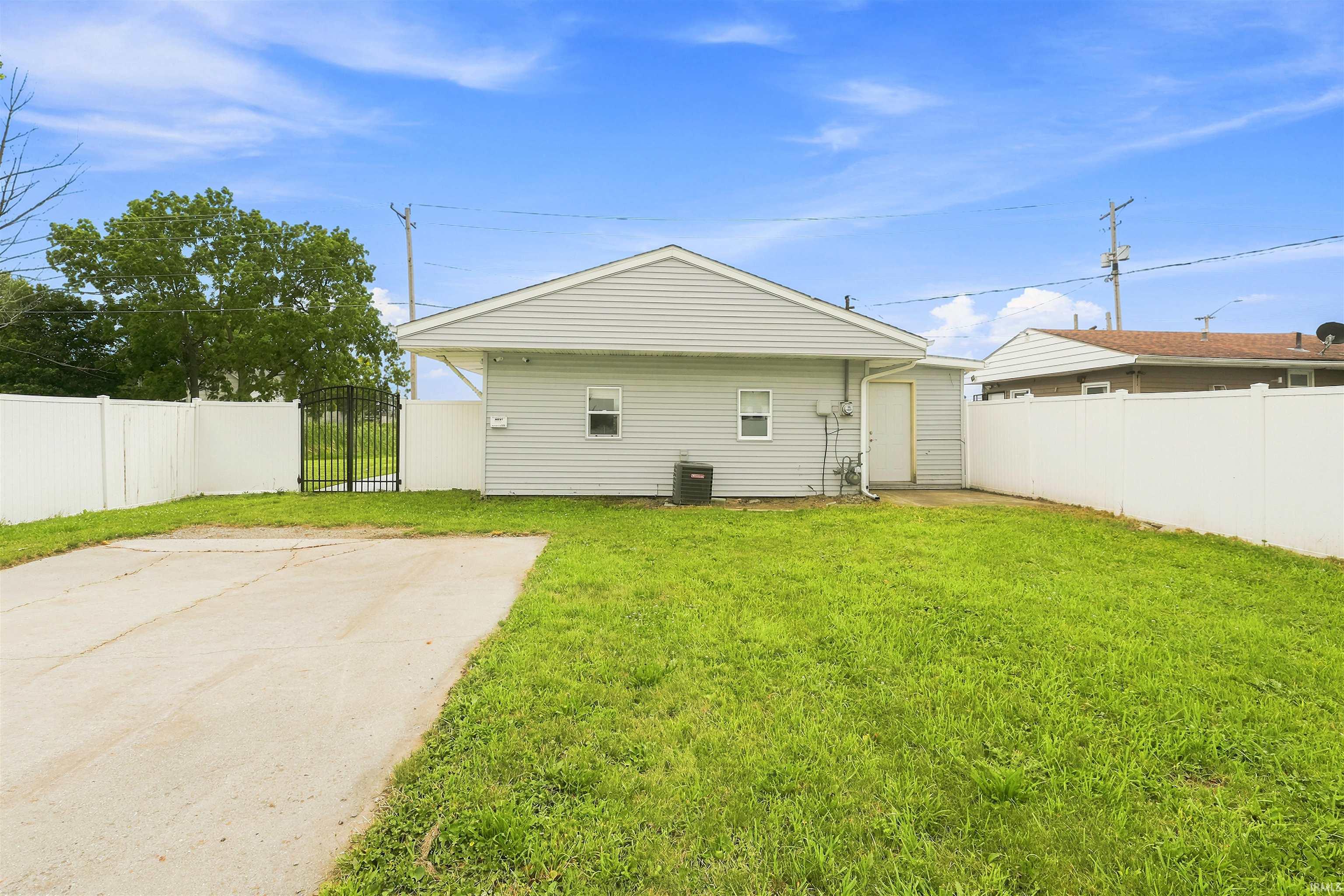 Fenced backyard featuring a concrete pad, mature lawn, and side access door
