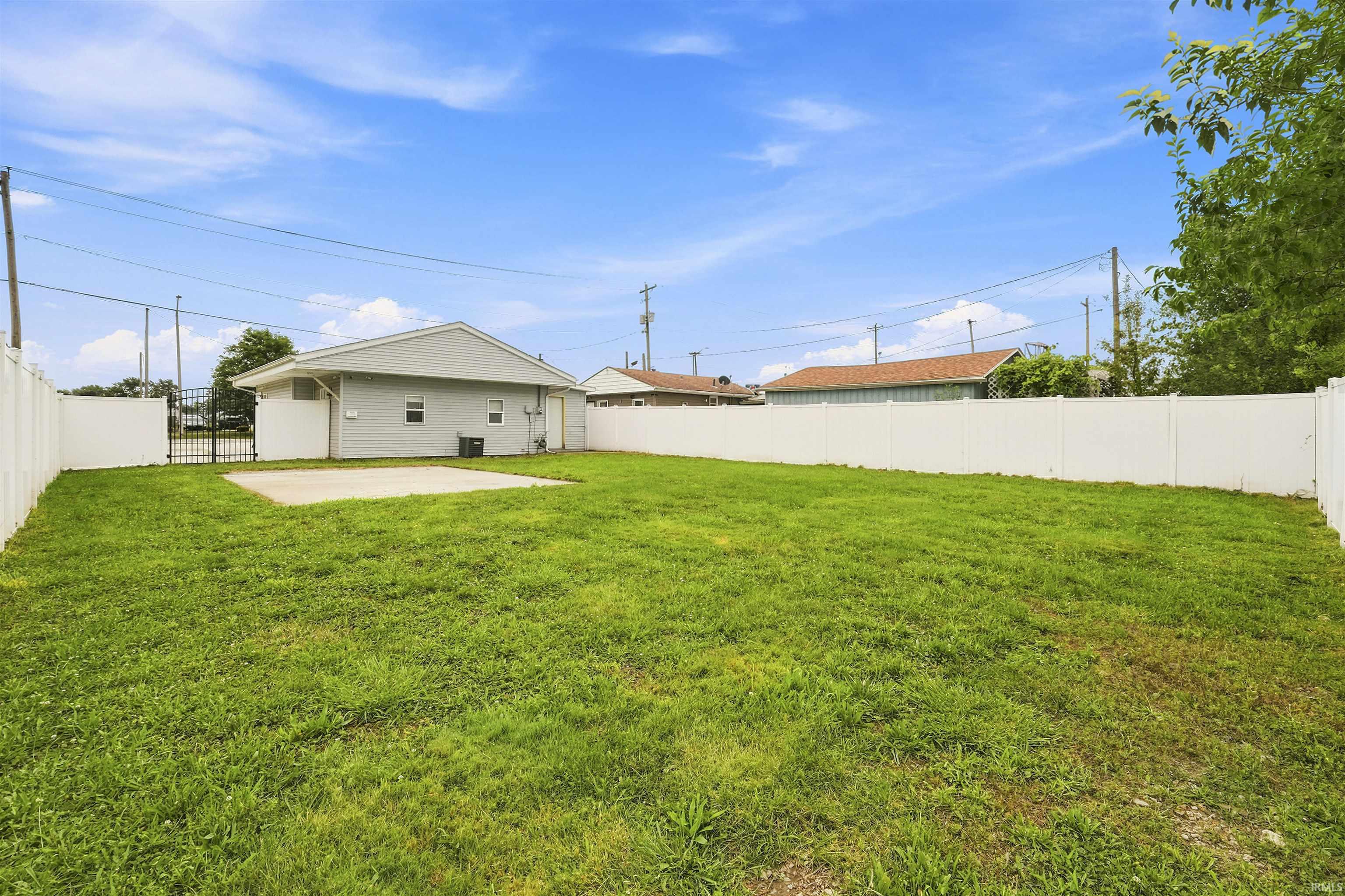 Expansive rear yard featuring a concrete patio, perimeter vinyl fencing, and a separate metal gate
