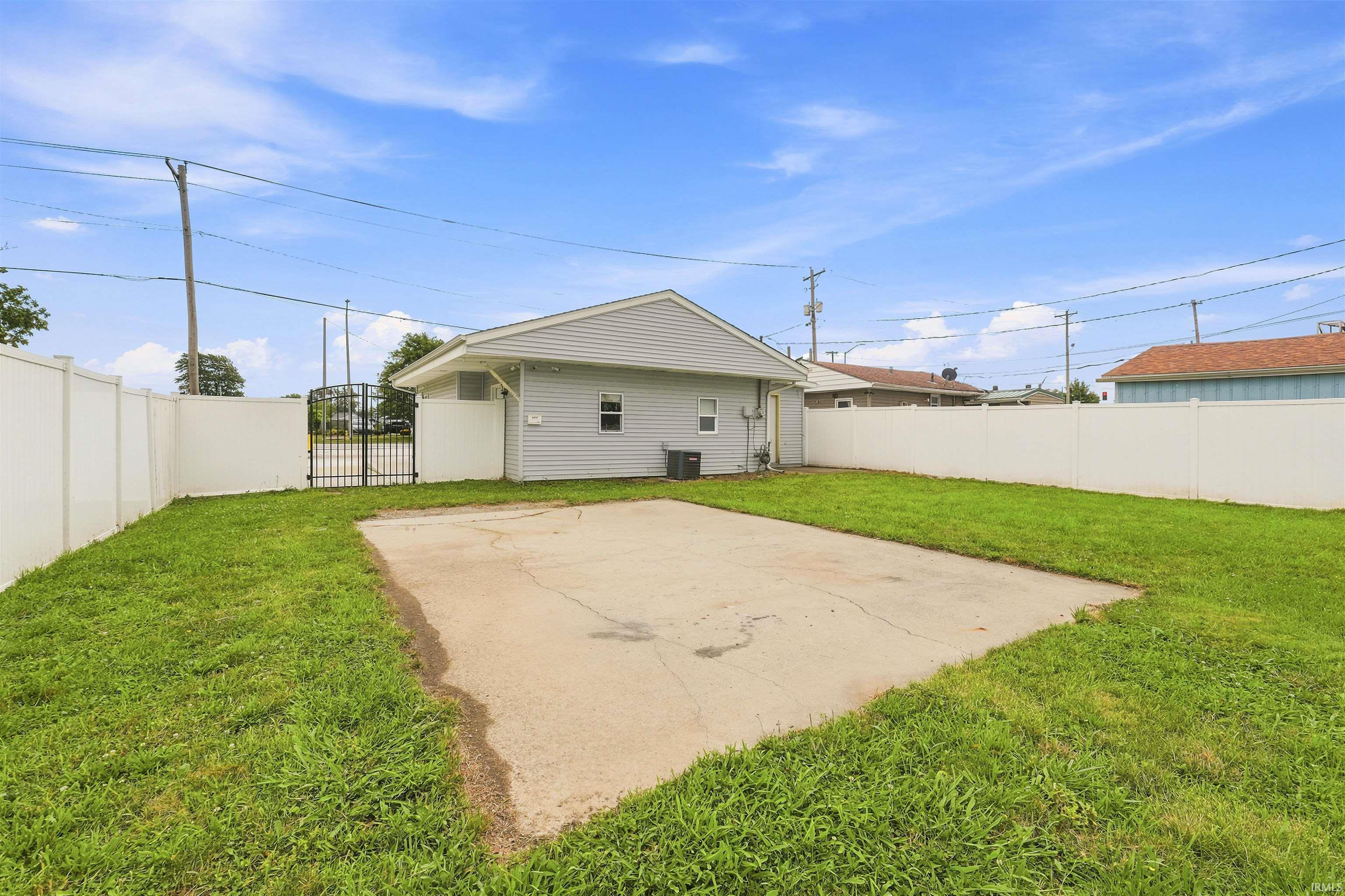 Expansive rear yard featuring a large concrete pad, privacy fencing, and a double gate entry