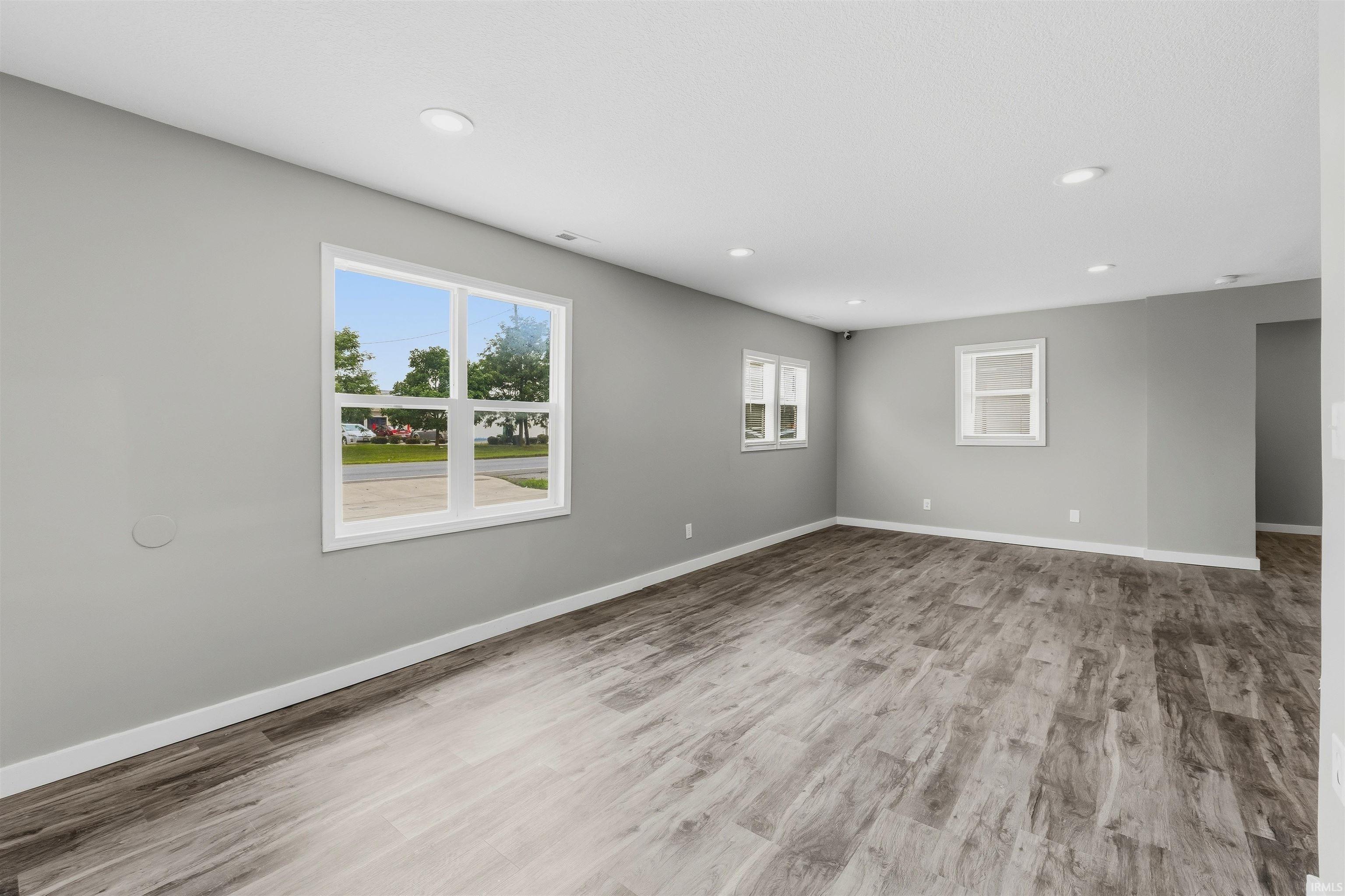 Spacious room featuring wood-finish flooring, recessed lighting, multiple windows, and a neutral wall palette