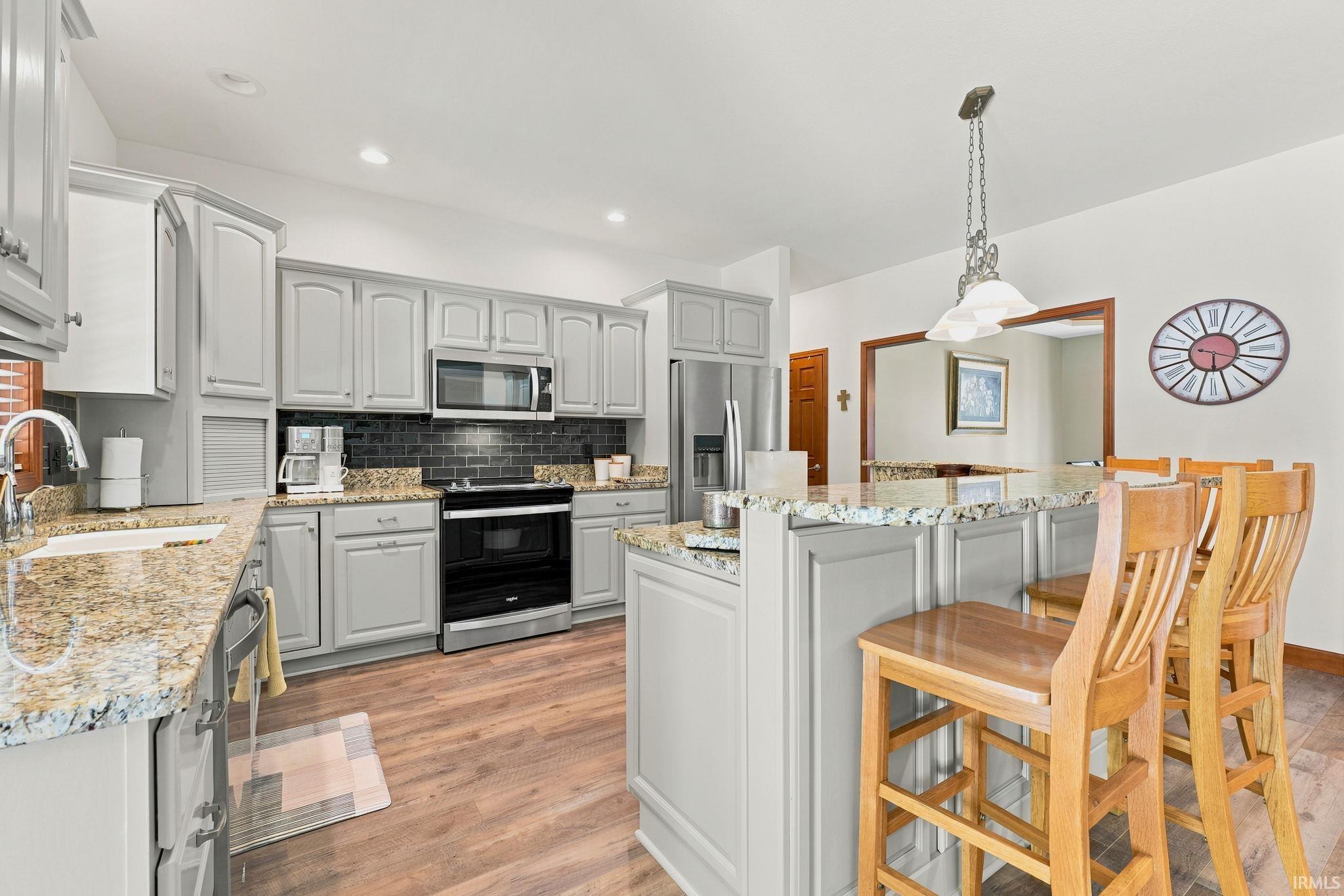 Kitchen featuring light gray cabinetry, granite countertops, wood-finish flooring, a black subway tile backsplash, and a stainless steel appliance suite