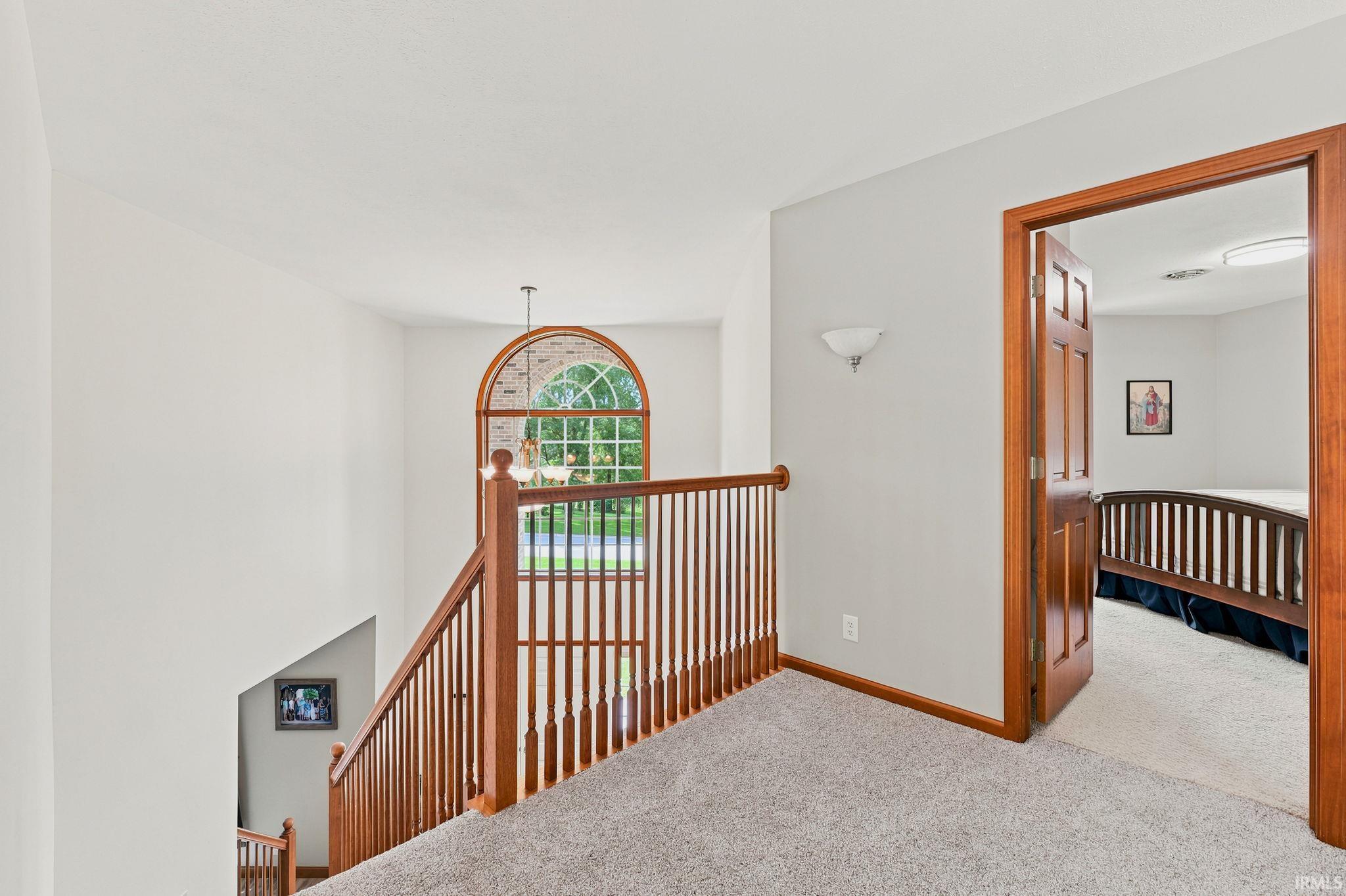 Upper-level landing featuring a wood staircase with balusters and a large arched window