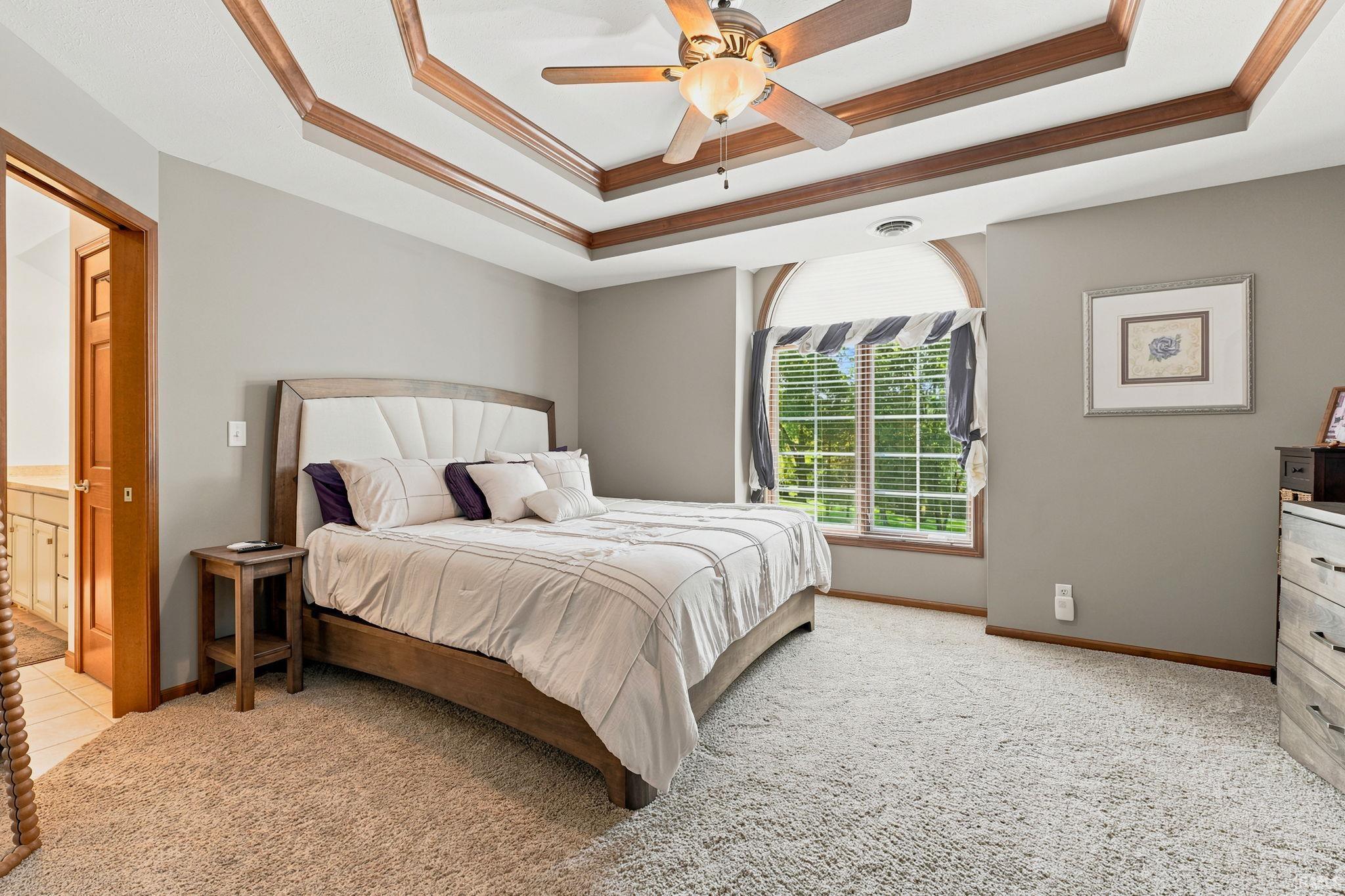 Spacious interior featuring a multi-tiered tray ceiling with rich wood accents, a ceiling fan, and light gray wall paint