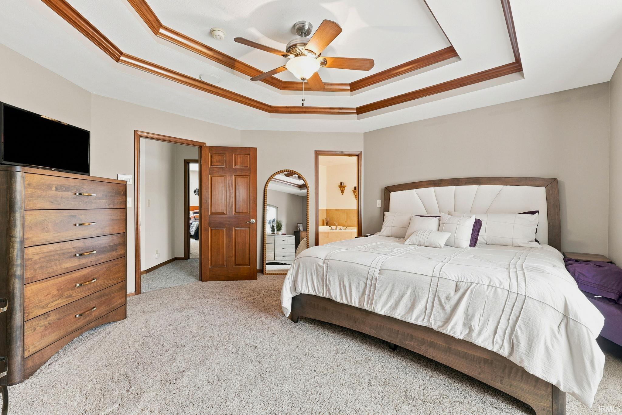 Bedroom featuring a multi-tiered tray ceiling with wood trim accents and a ceiling fan with integrated lighting